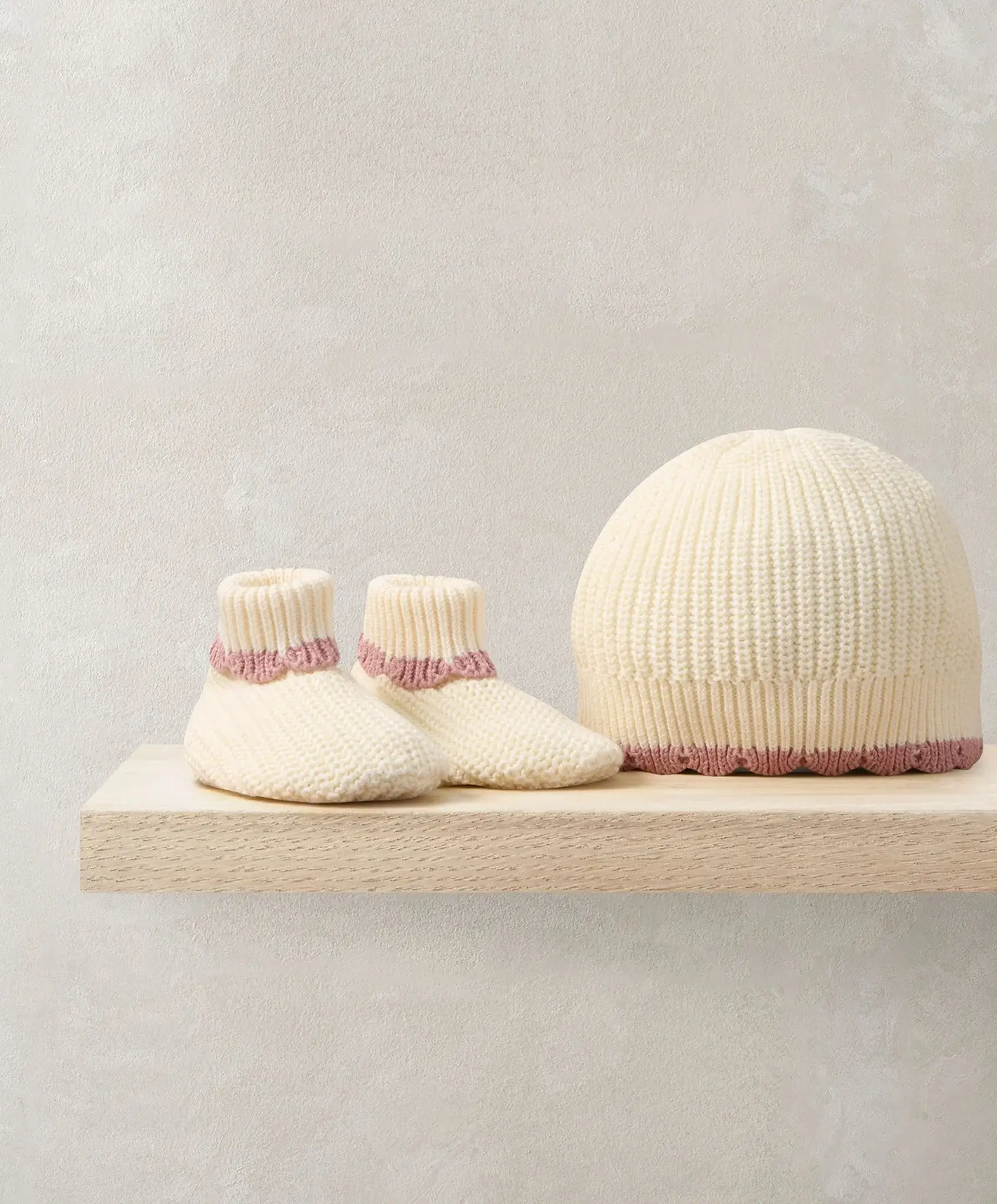 Knitted baby booties and a matching hat on a wooden shelf.