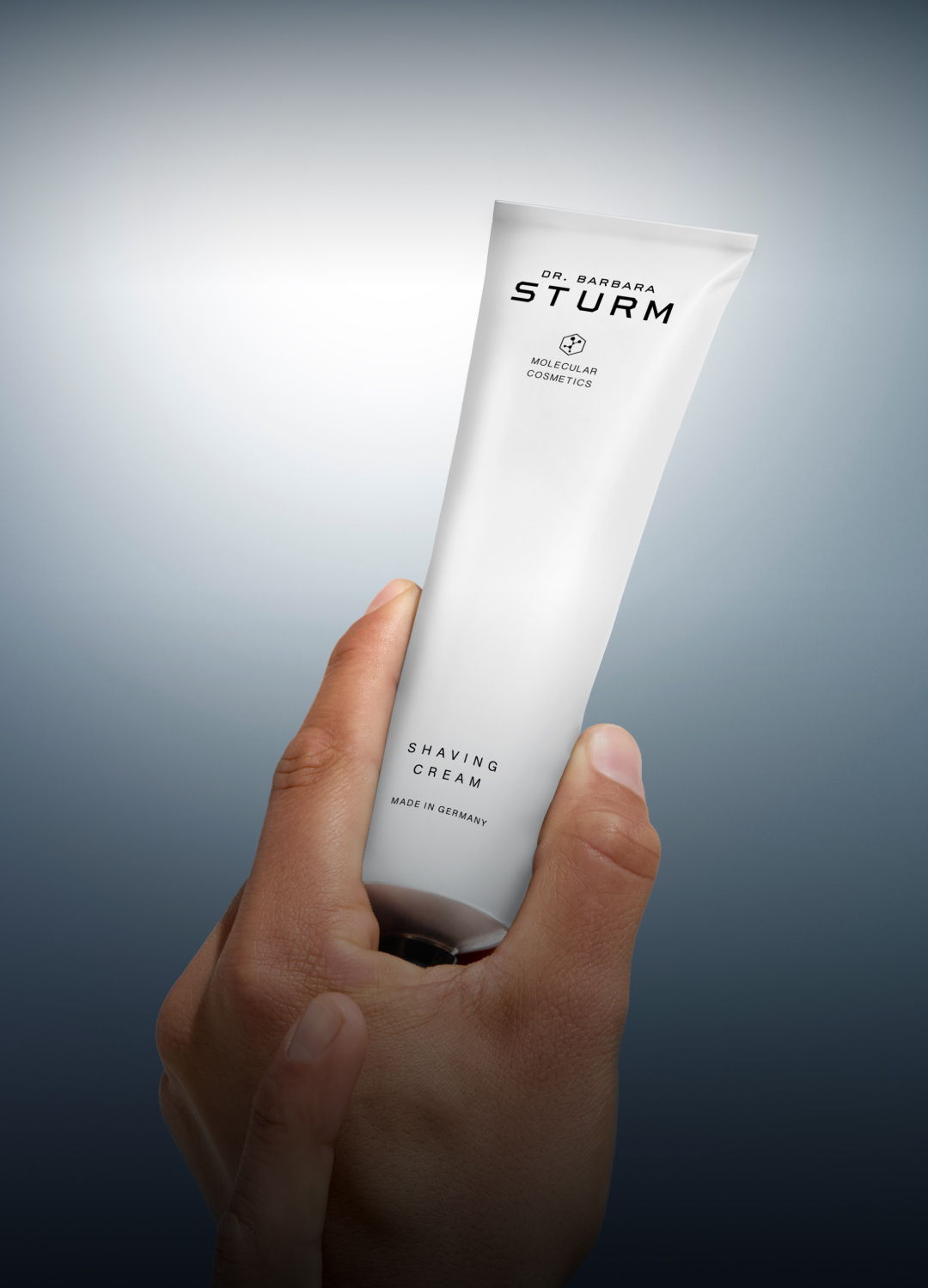 Hand holding a tube of skincare cream against a blurred background.
