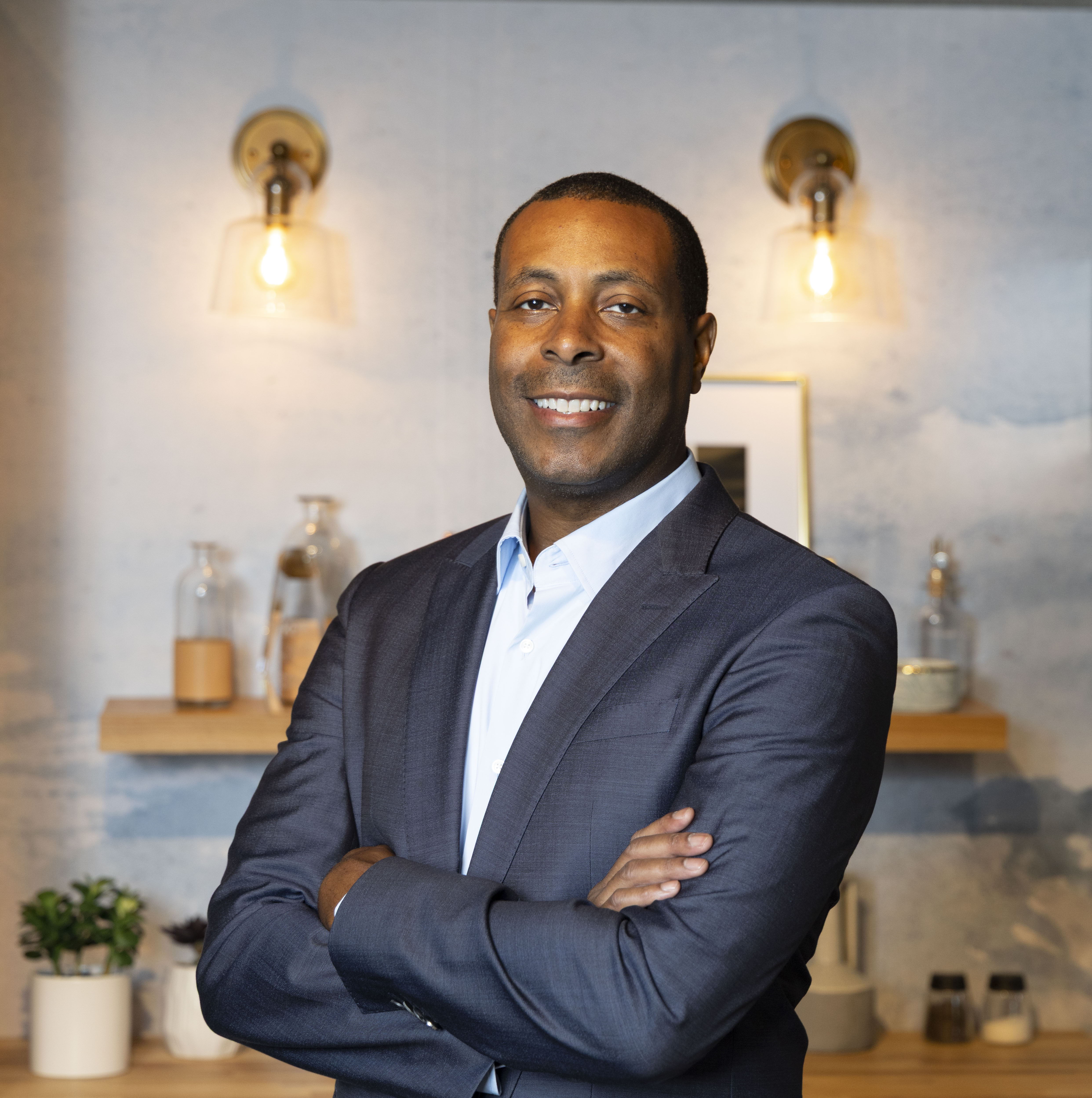 Smiling man in a business suit with arms crossed, standing indoors.