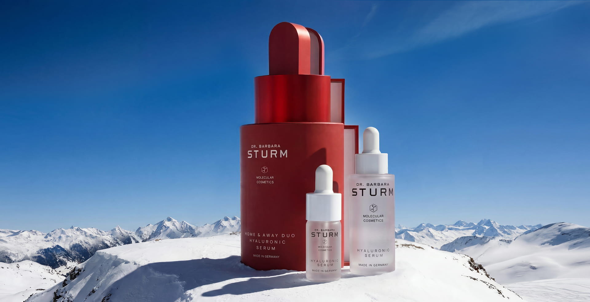 Skin care products displayed against a snowy mountain backdrop under a clear blue sky.