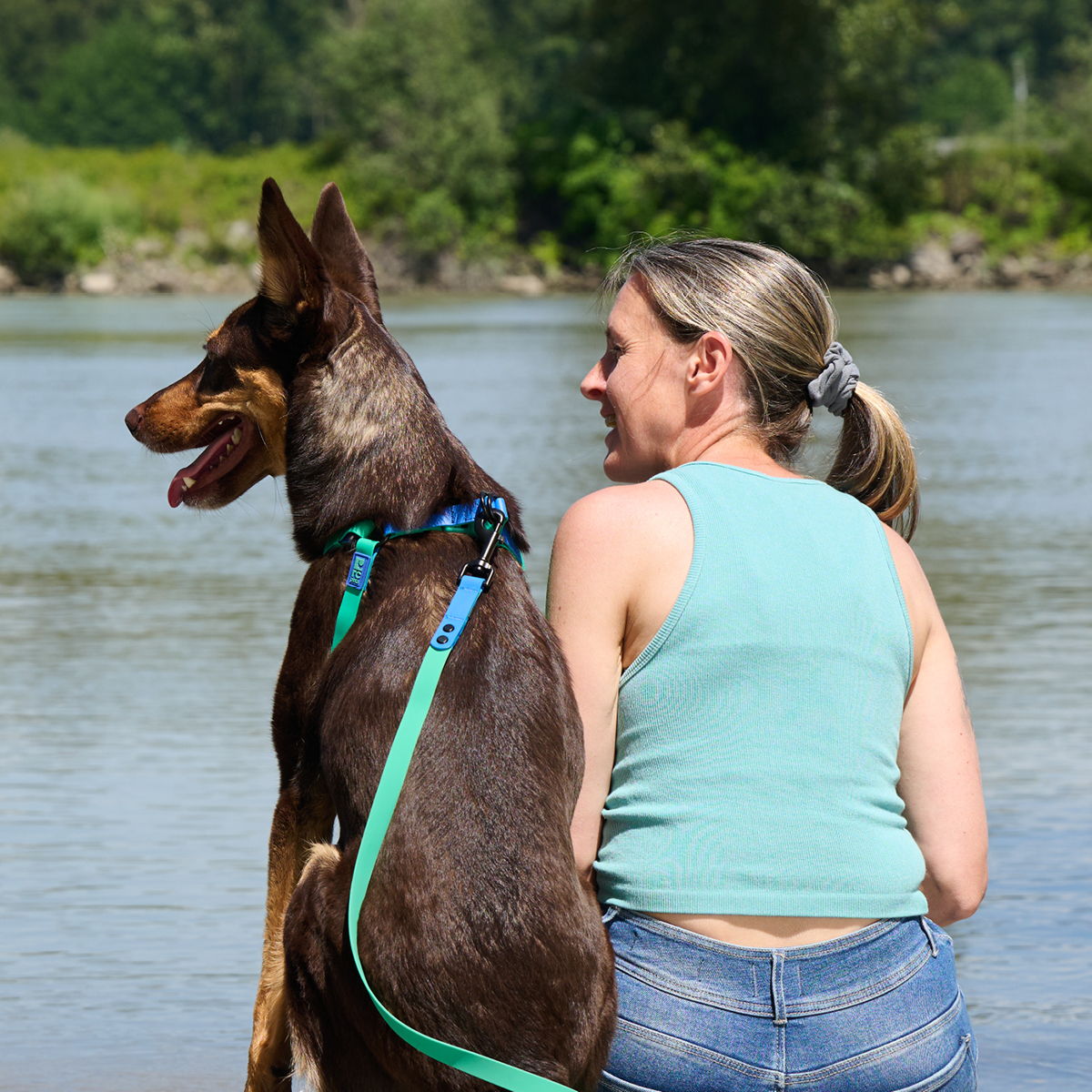 Woman sitting by the river with a dog, both looking out at the water.