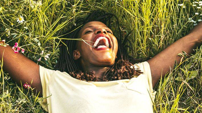 A woman laying down laughing in a field- Babo Botanicals