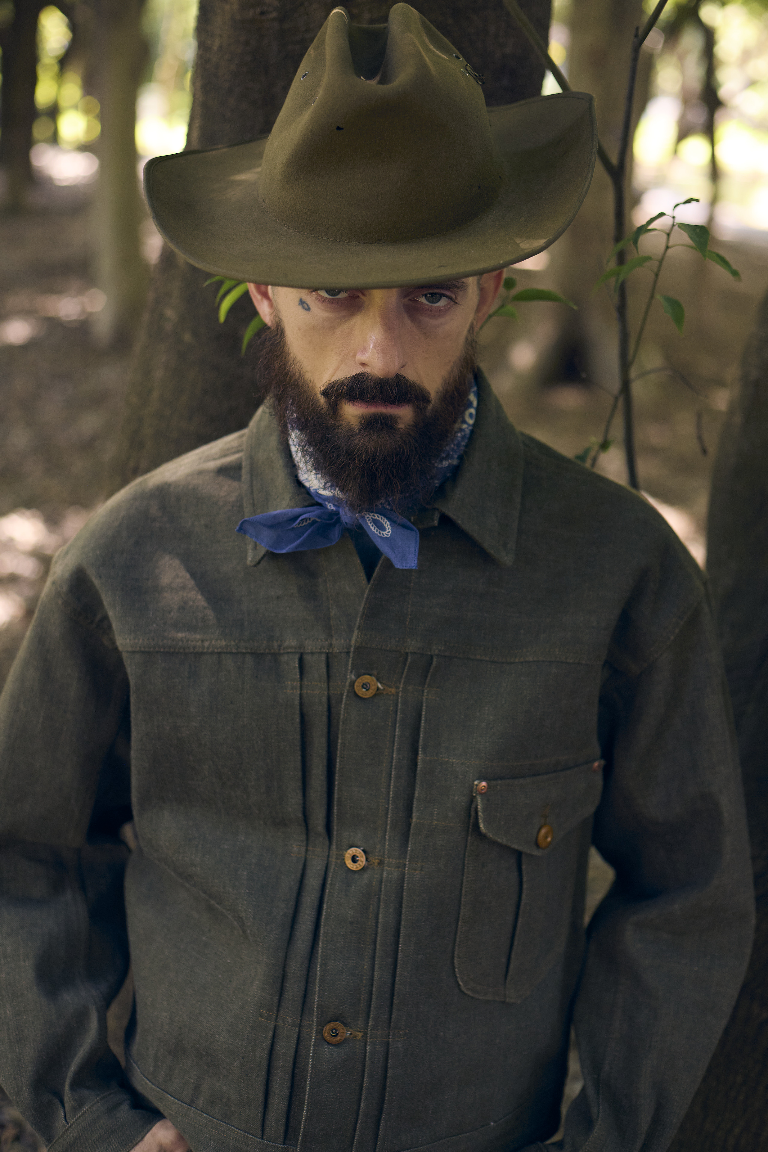 Man wearing a hat and jacket, standing among trees.