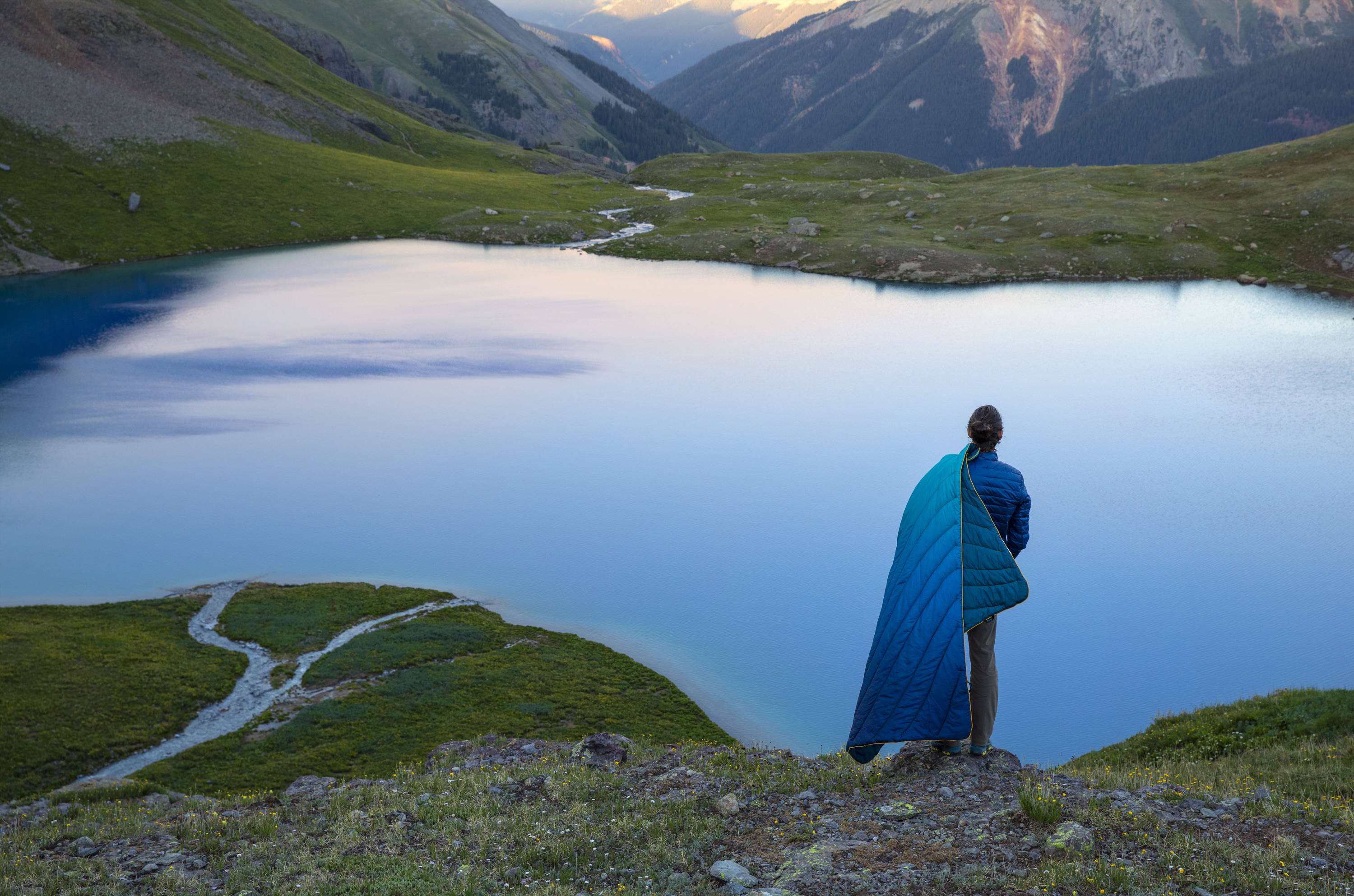 Person exploring and holding the Rumpl Ocean Fade Puffy Blanket overlooking nature in the Pacific Northwest