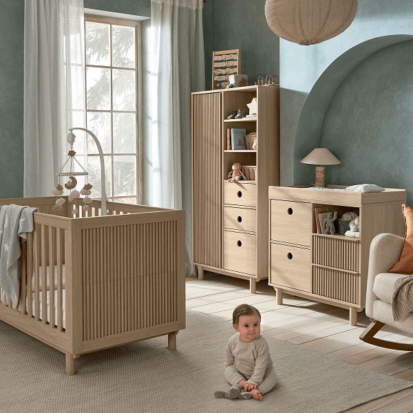 A cozy nursery with a crib, child, and wooden furniture.