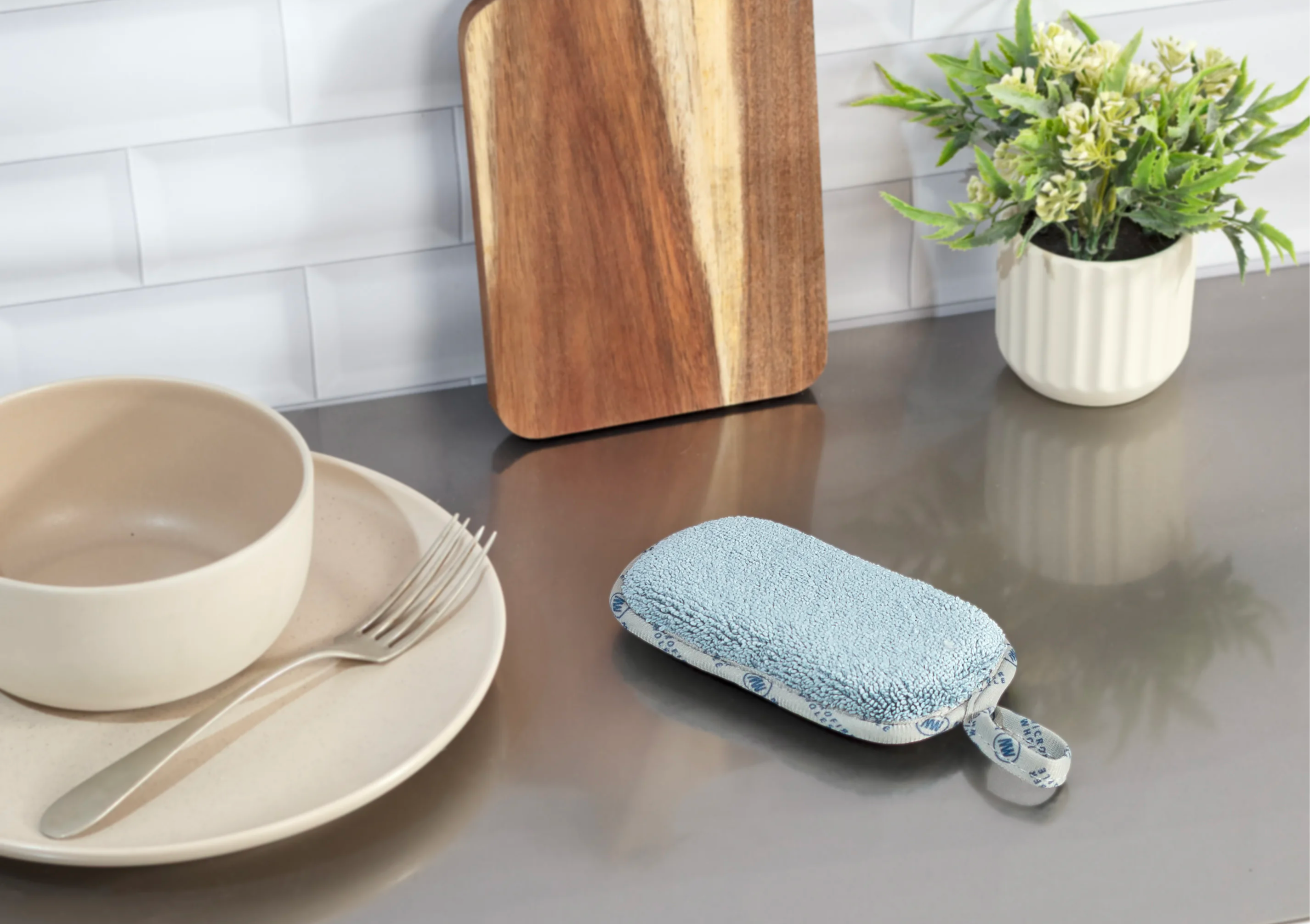A wooden cutting board, bowls, utensils, and a small plant on a countertop.