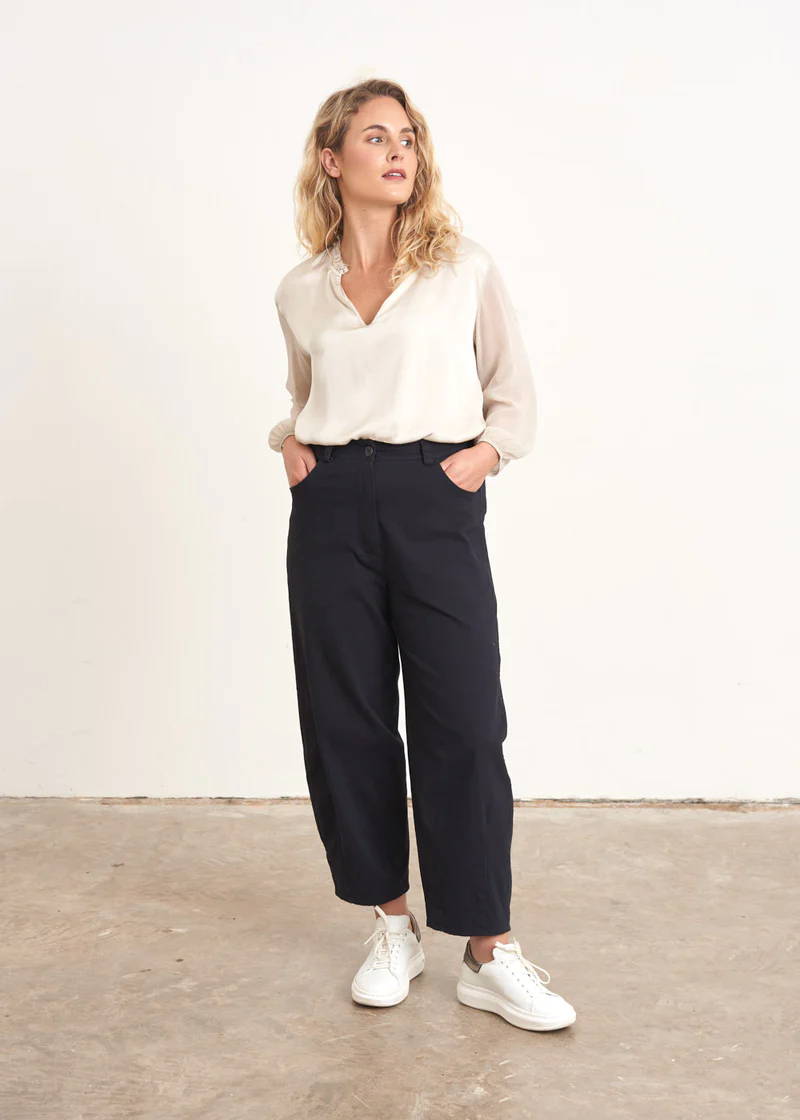A model wearing a pair of blue black barrel leg trousers with an off white top and white trainers