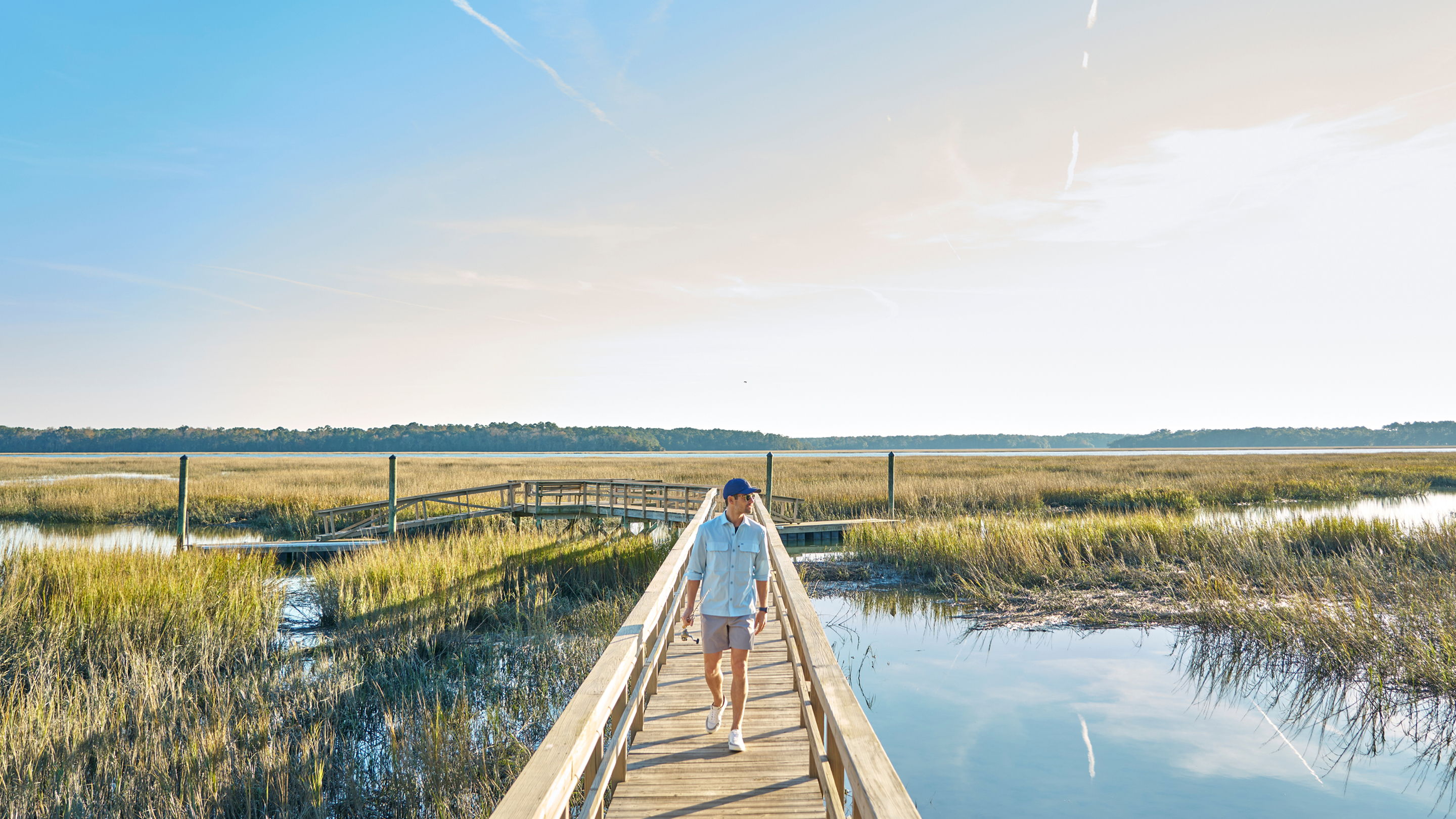 Person walking on a wooden boardwalk through a marsh landscape.
