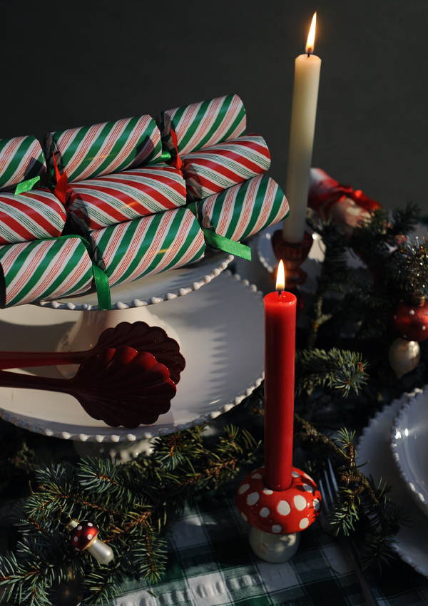 Three christmas crackers set on a stack of plates on a laid christmas table.