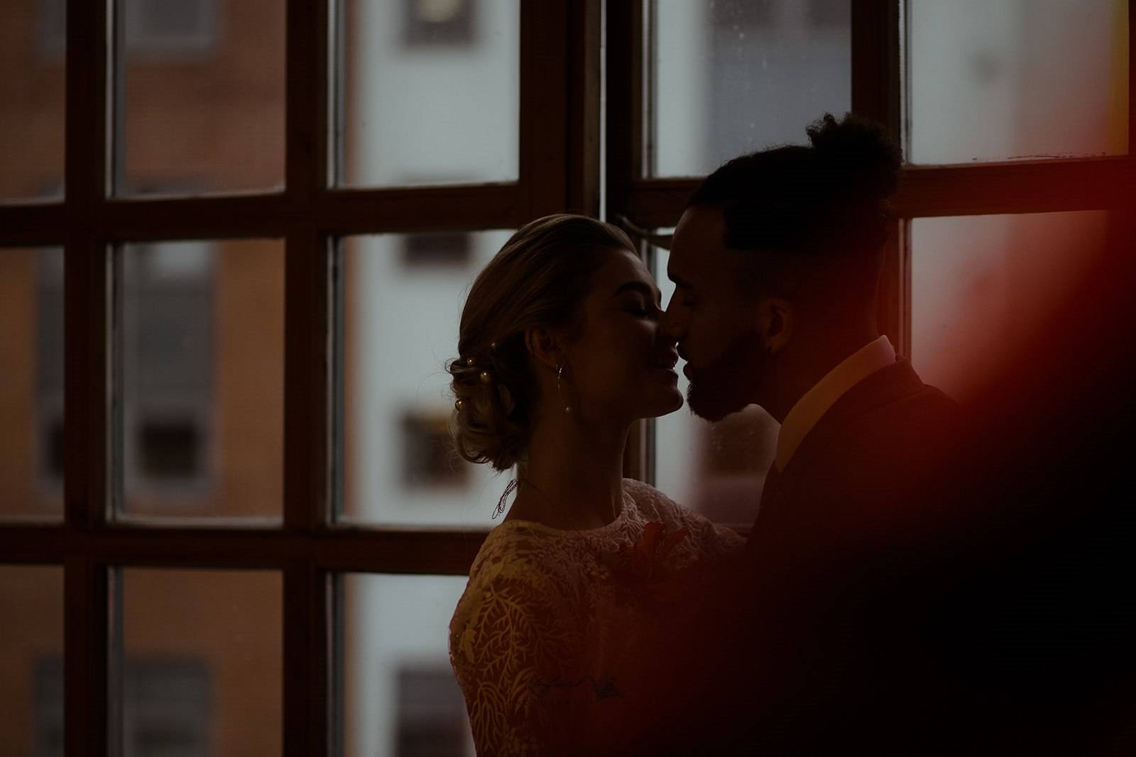 Image shows a couple about to kiss in front of a window, taken by Unfurl Photography Newcastle