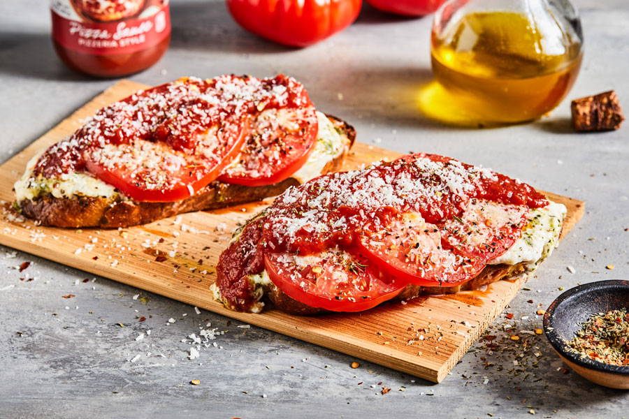 Toast with melty cheese, tomatoes and red pizza sauce served on a wood plank