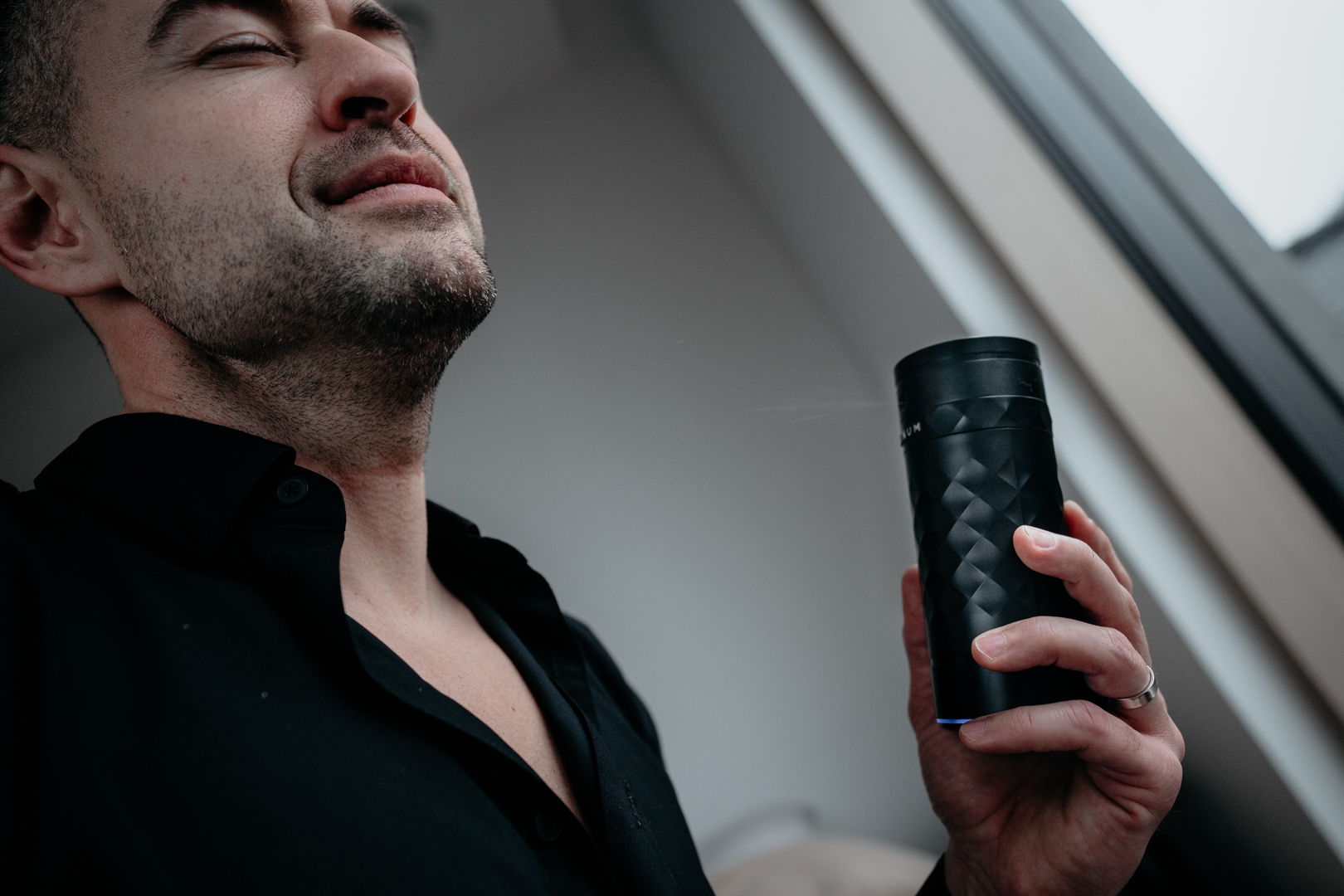 Man holding a black object, eyes closed, in a well-lit room.