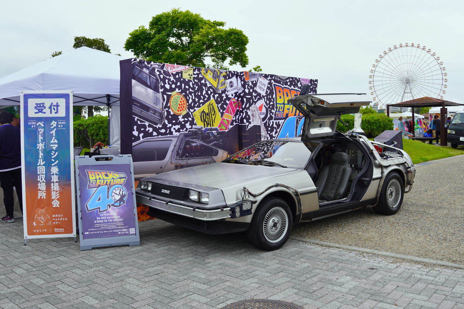 A DeLorean car with its doors open, set at an outdoor event.