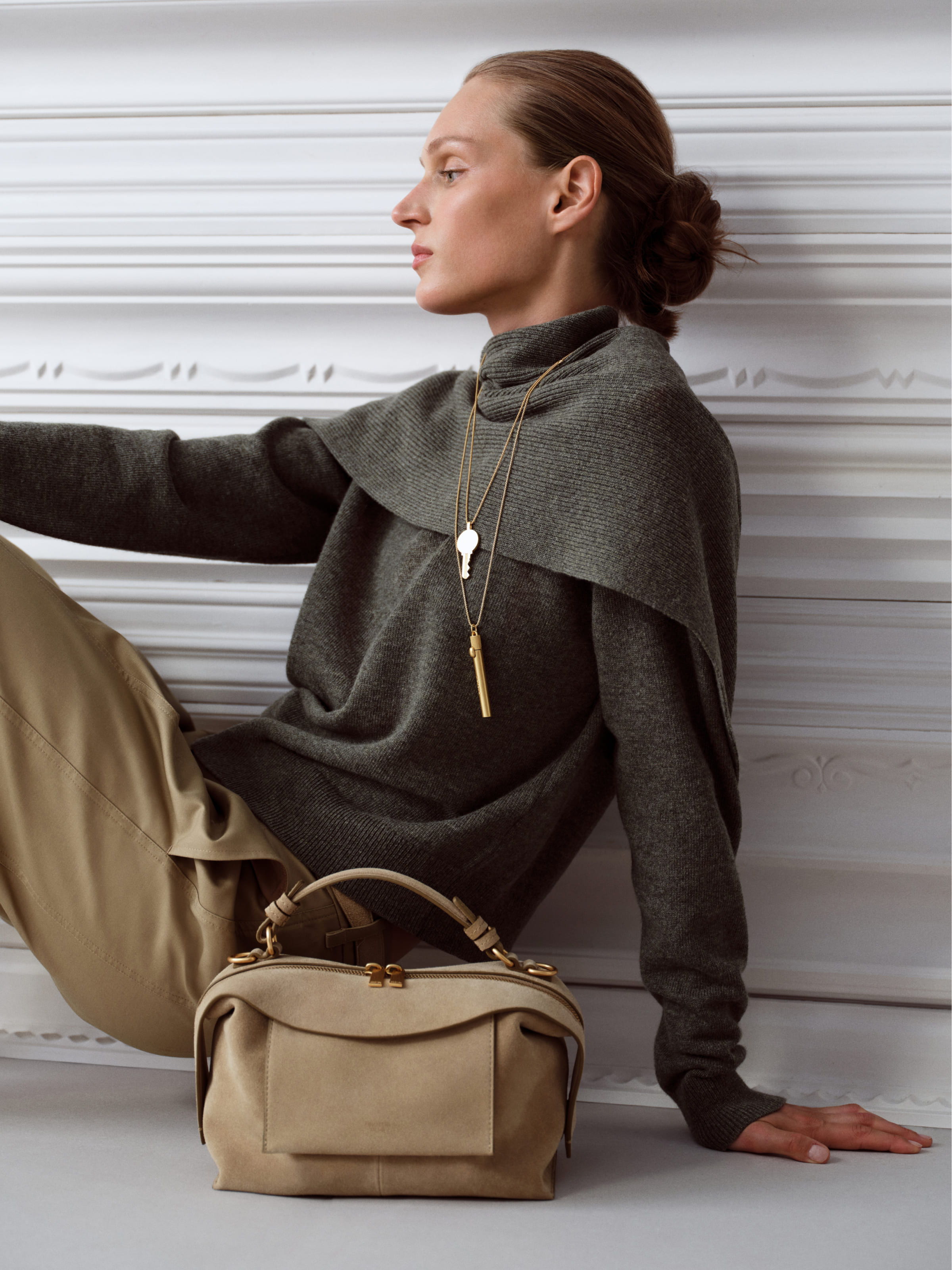 Woman in stylish outfit poses with a handbag against a textured background.
