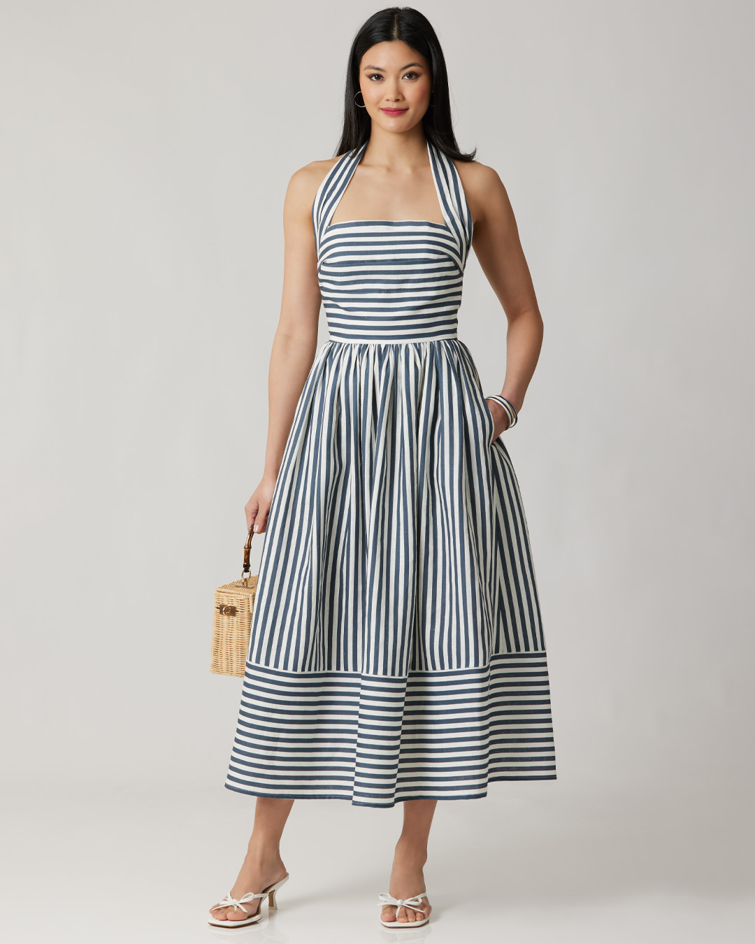 A woman wearing a striped halter dress, holding a small handbag.
