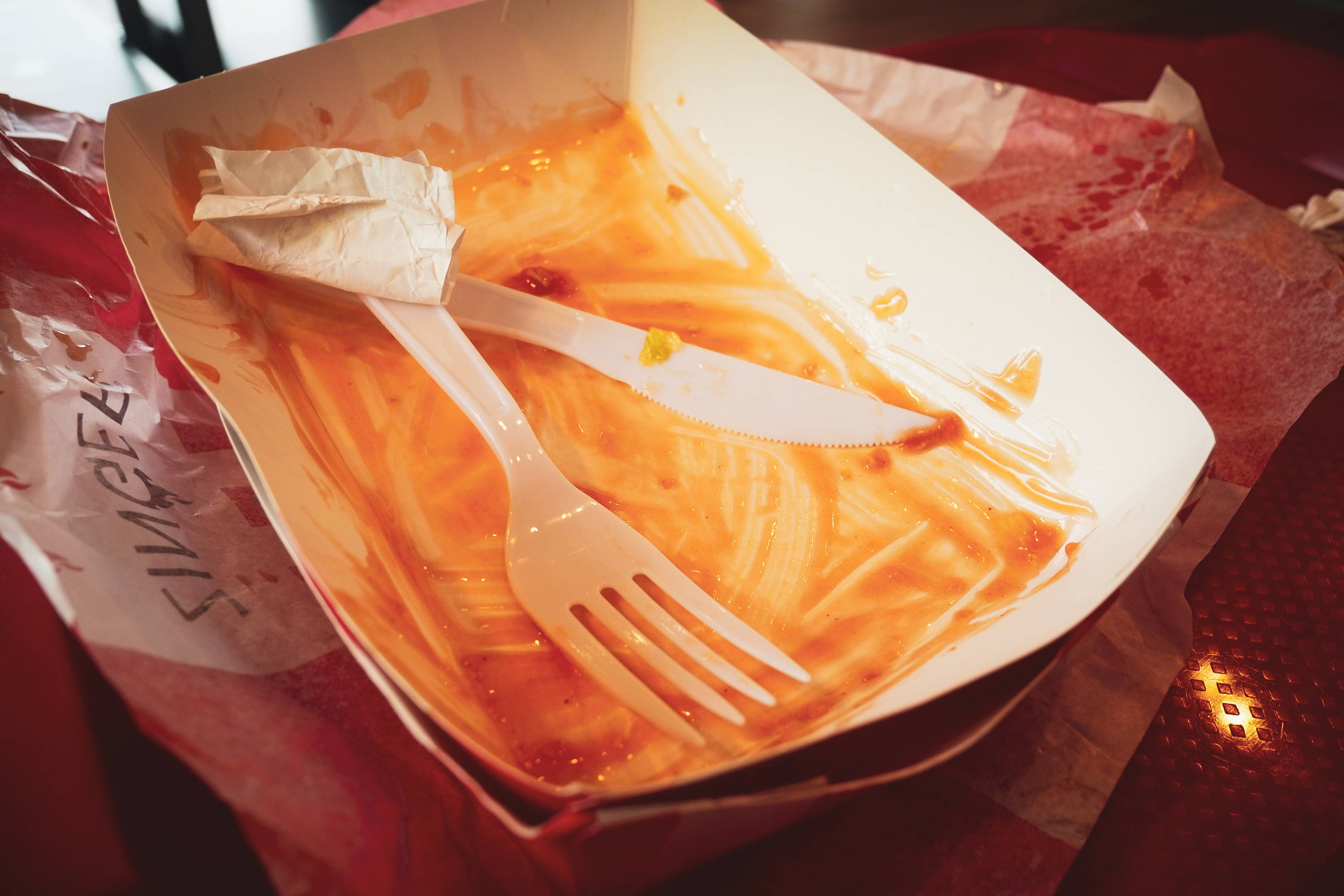 Paper food trays and plastic cutlery soiled with sauce and food scraps