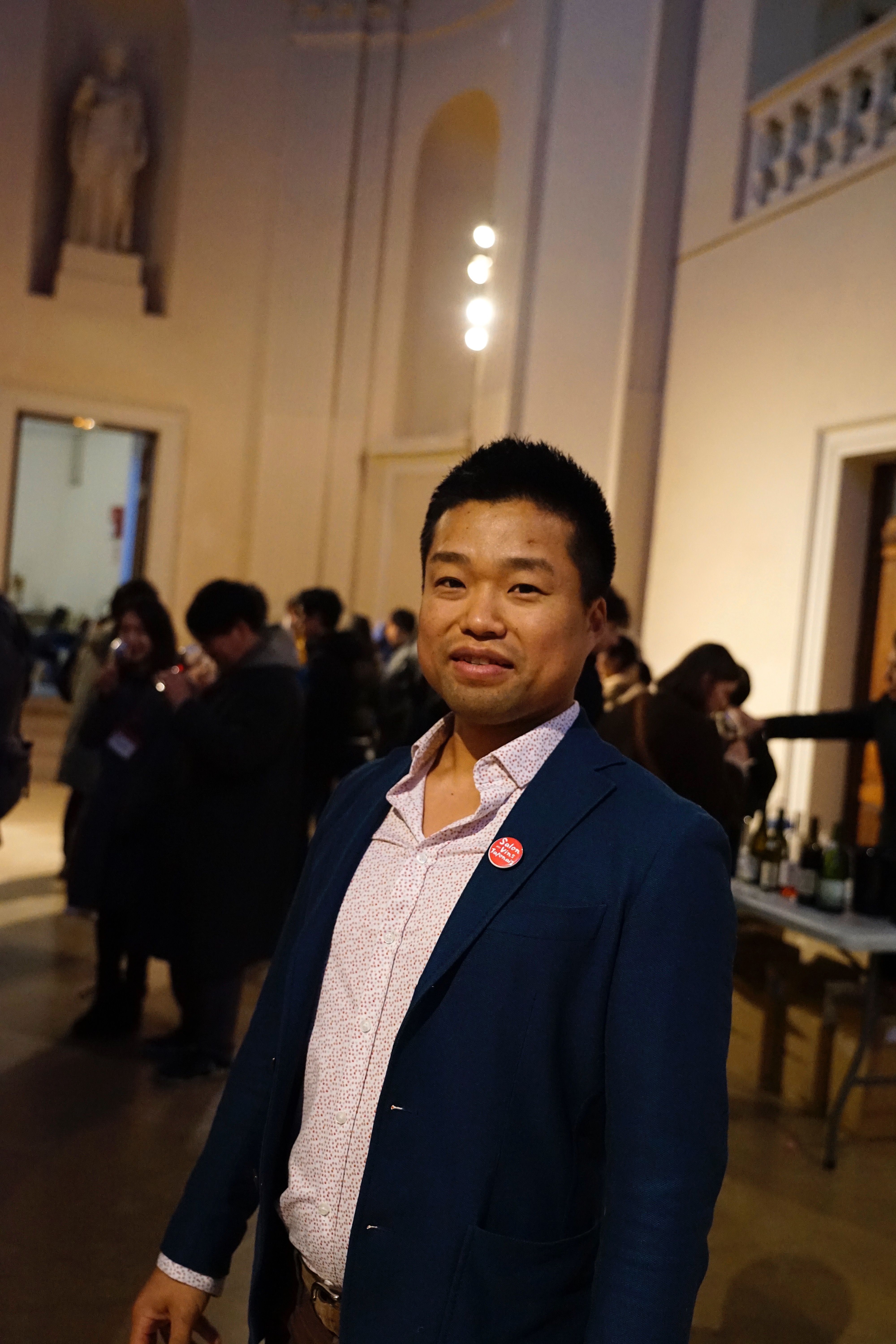 A man in a blue blazer stands in a crowded indoor space.
