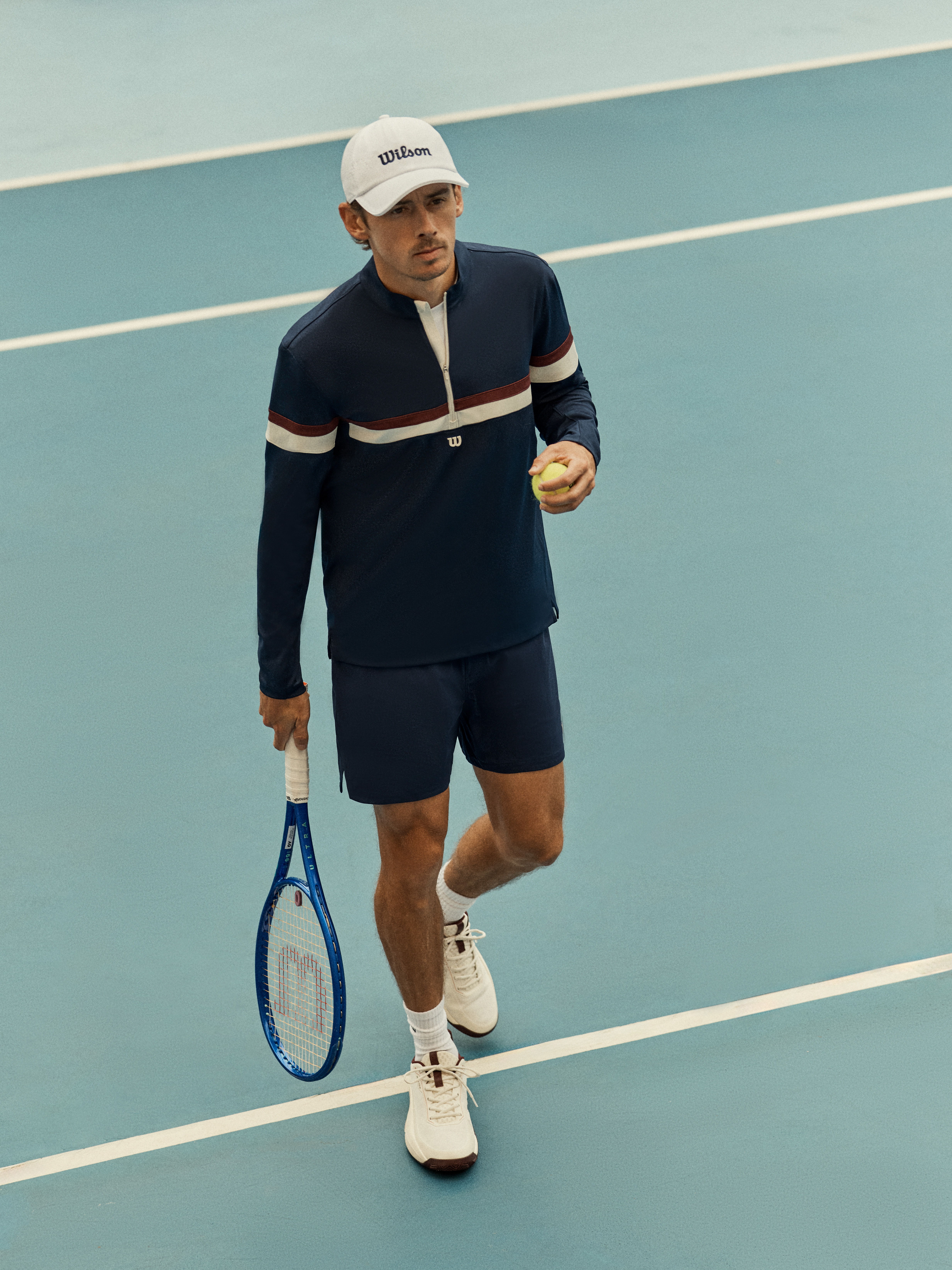 Man in sportswear holding a tennis ball and racket on a court.