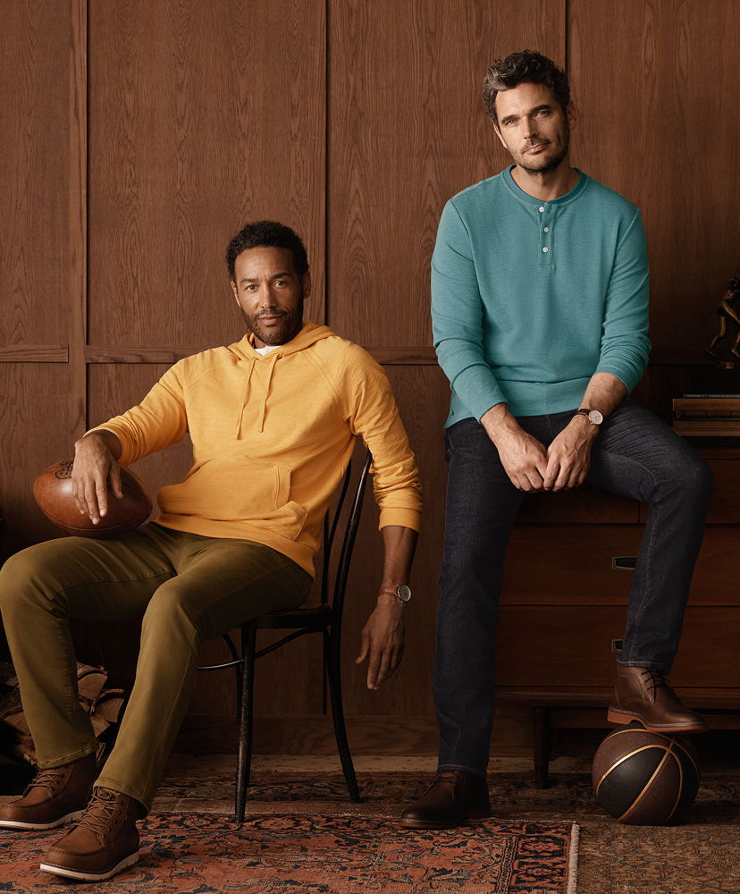 Two men in casual outfits posing with sports equipment indoors.