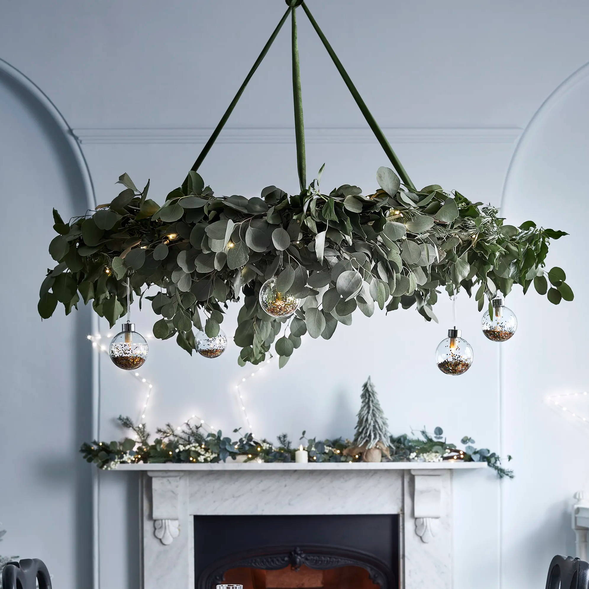 Foliage chandelier feature hanging from dining room ceiling with mantel in background featuring a festive garland, star light and mini tree