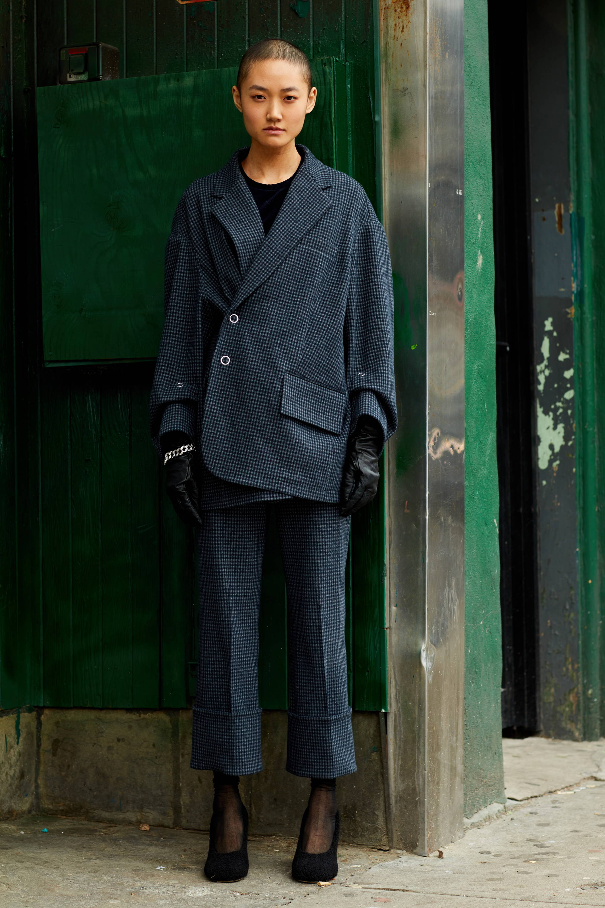Person in oversized suit standing against a green wall.
