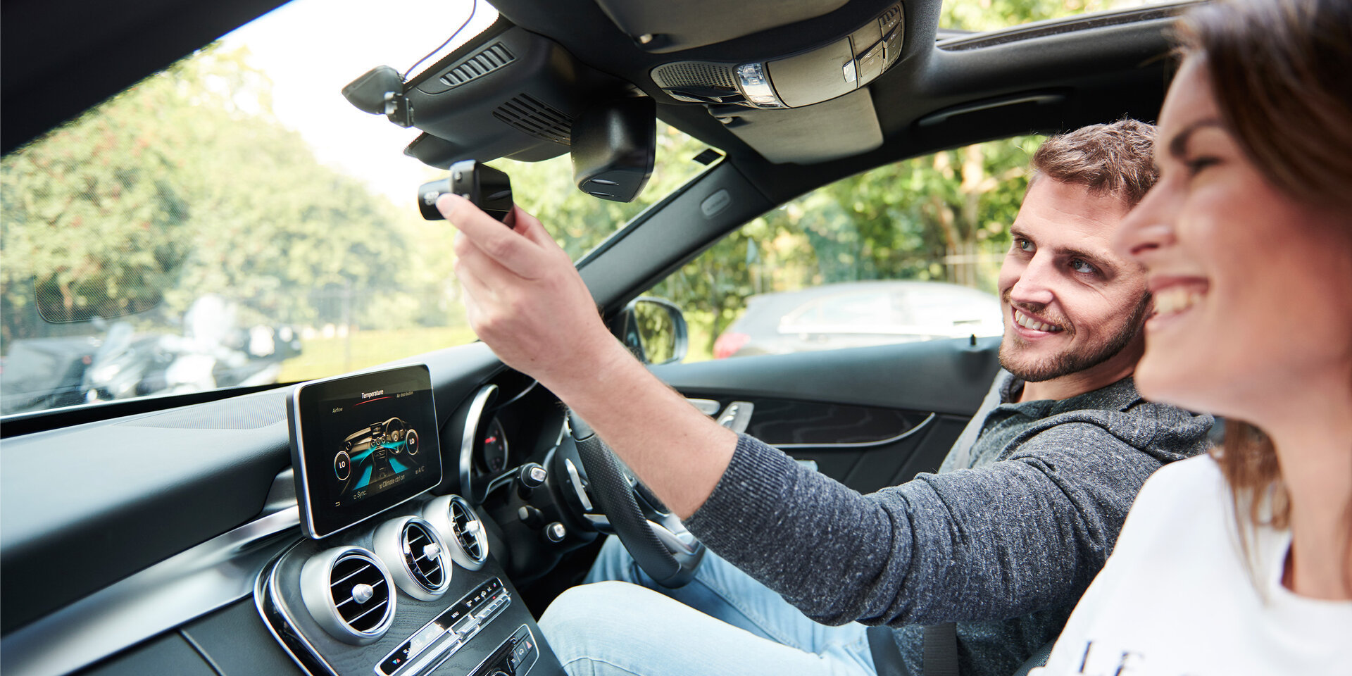 Driver attaching a Nextbase dash cam to the windshield inside a modern car.