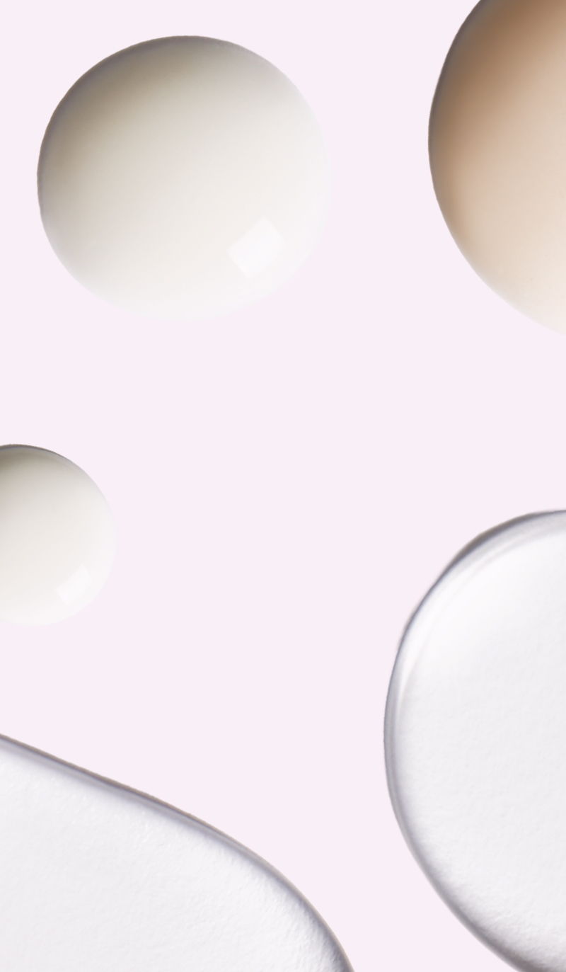 Drops of various colored liquids on a soft pink background.