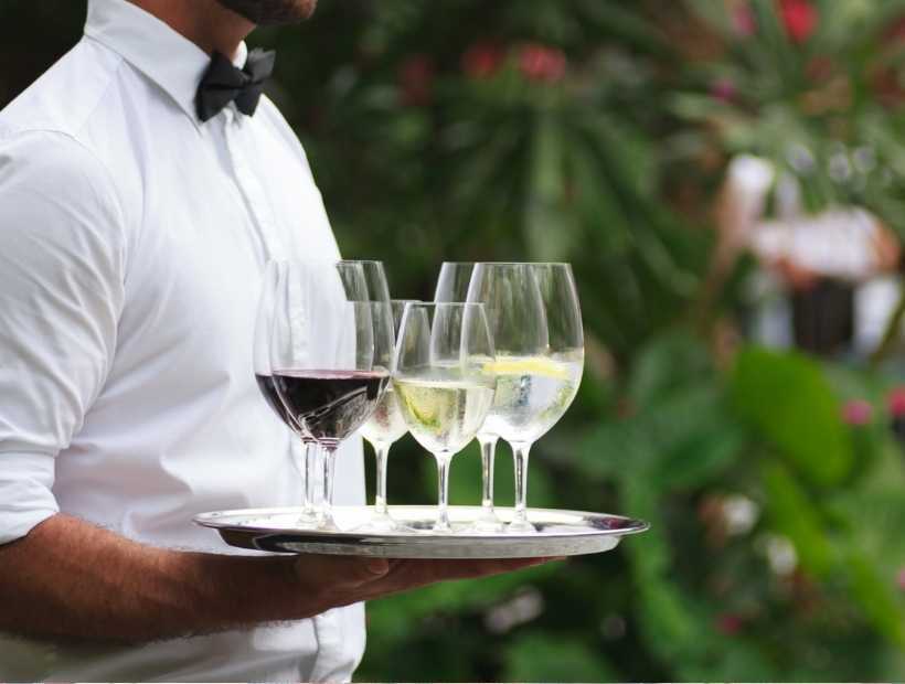 A waiter wearing a white button down and bow tie while carrying wine glasses