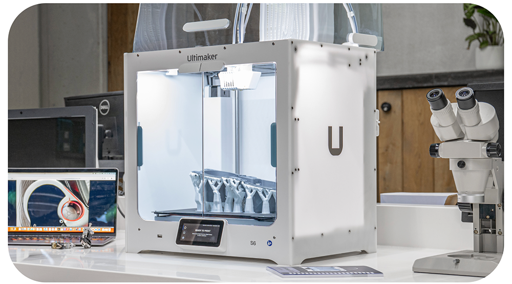 3D printer displayed on a table with microscope and digital screen nearby.