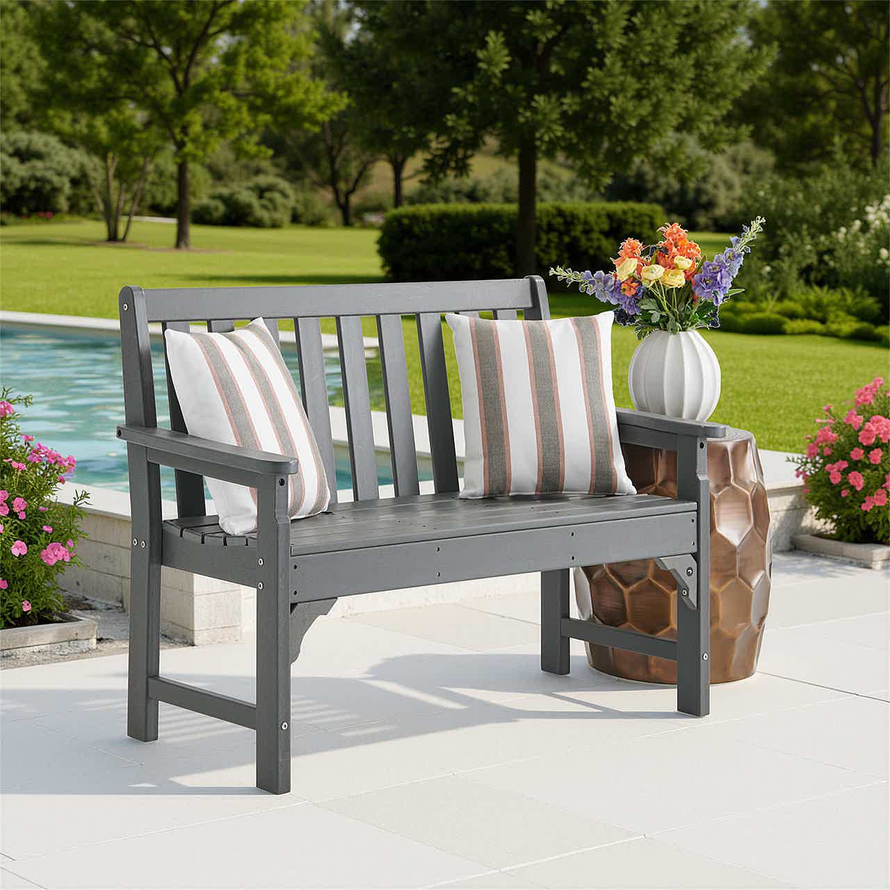 Outdoor bench with striped cushions and flowers near a pool.