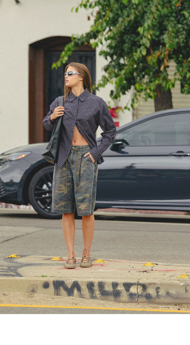 A person in casual attire stands on a sidewalk near a car.