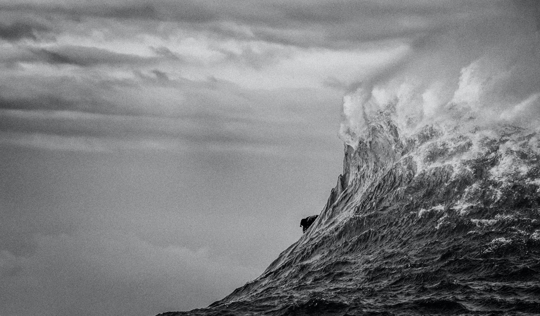Surfer shown taking off from behind the peak of a huge wave