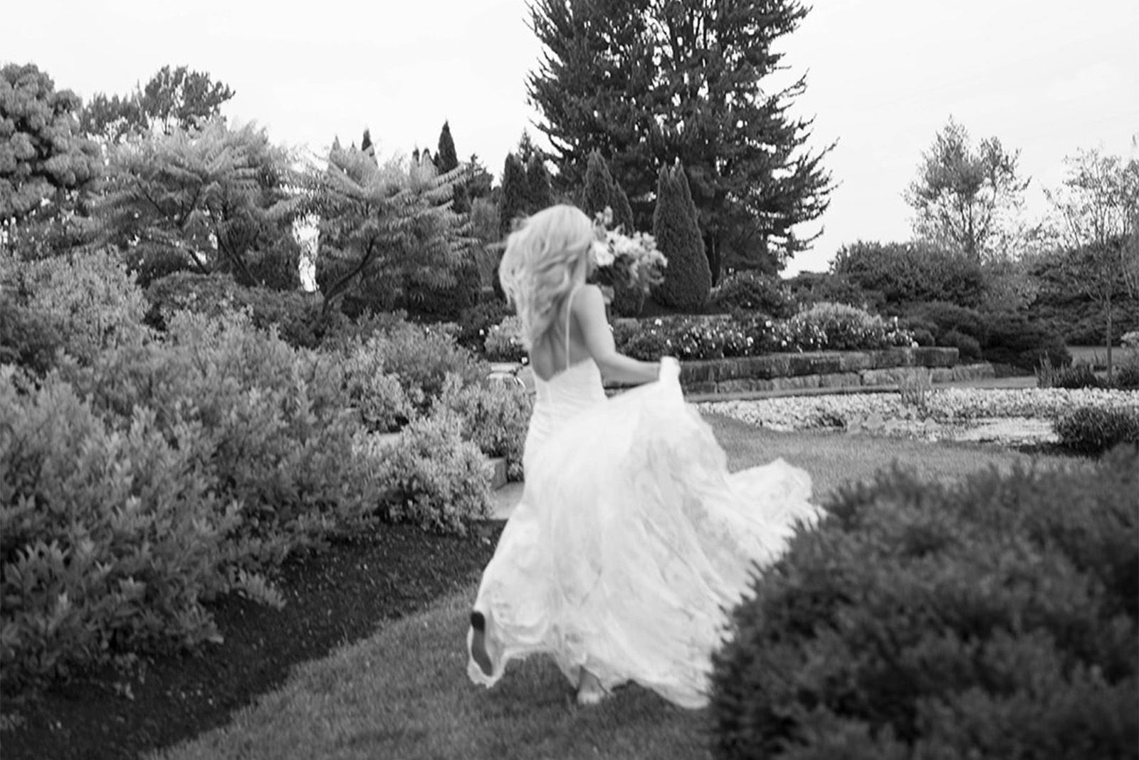 Bride in a flowing white dress running through a lush garden.