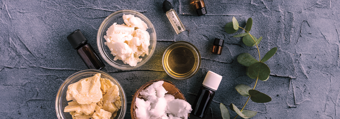Bowls of creams and oils with eucalyptus leaves on a textured surface.