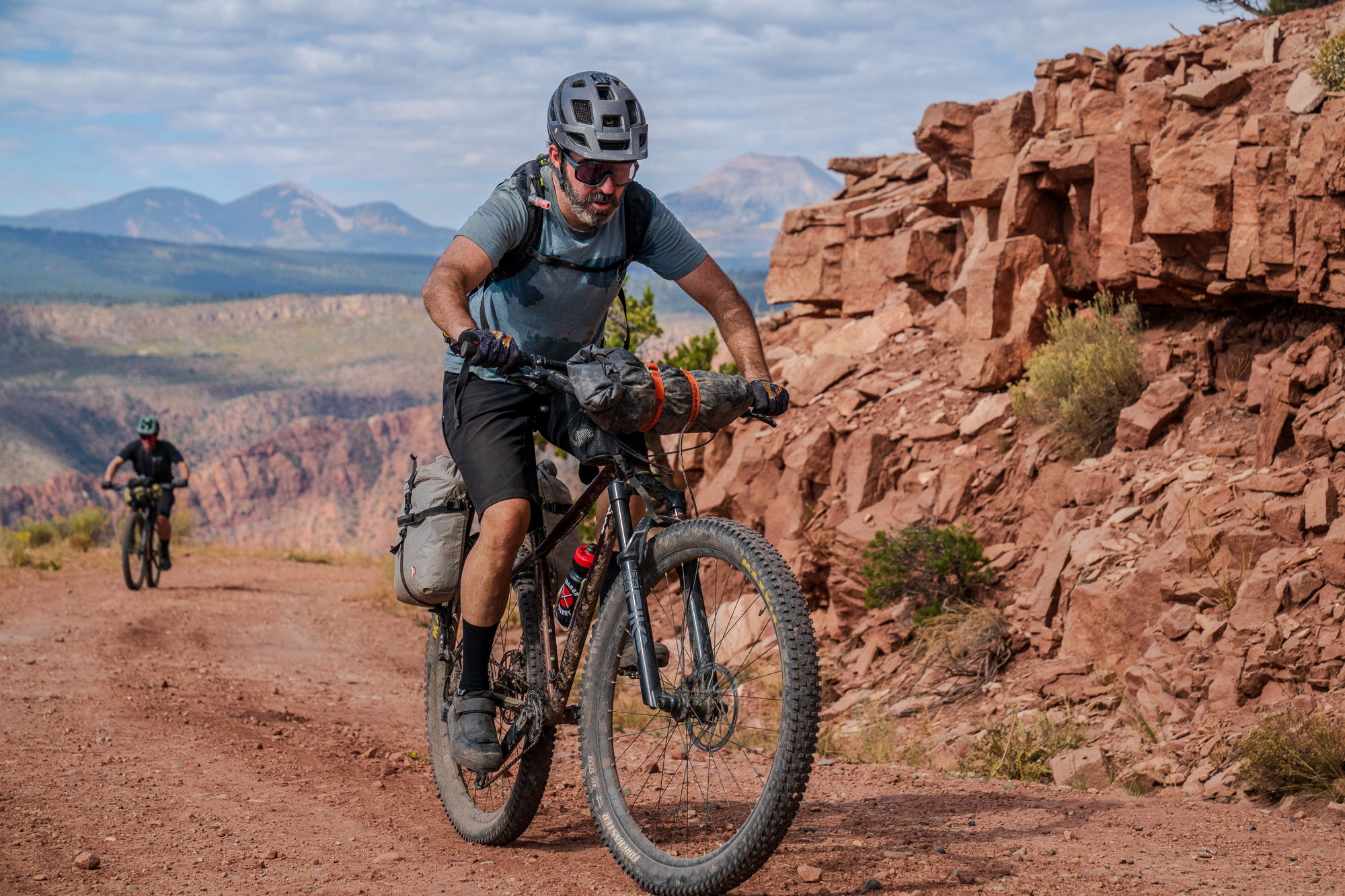 Person biking on a dirt path with rocky terrain and mountains of Utah in the background.