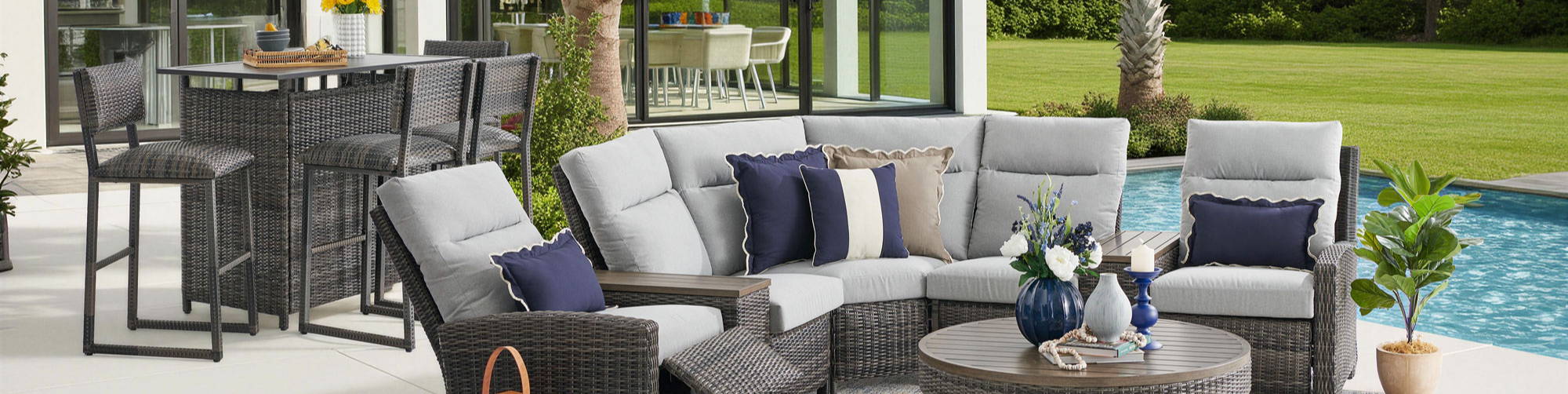 Outdoor seating area with sectional sofa and coffee table by a pool.