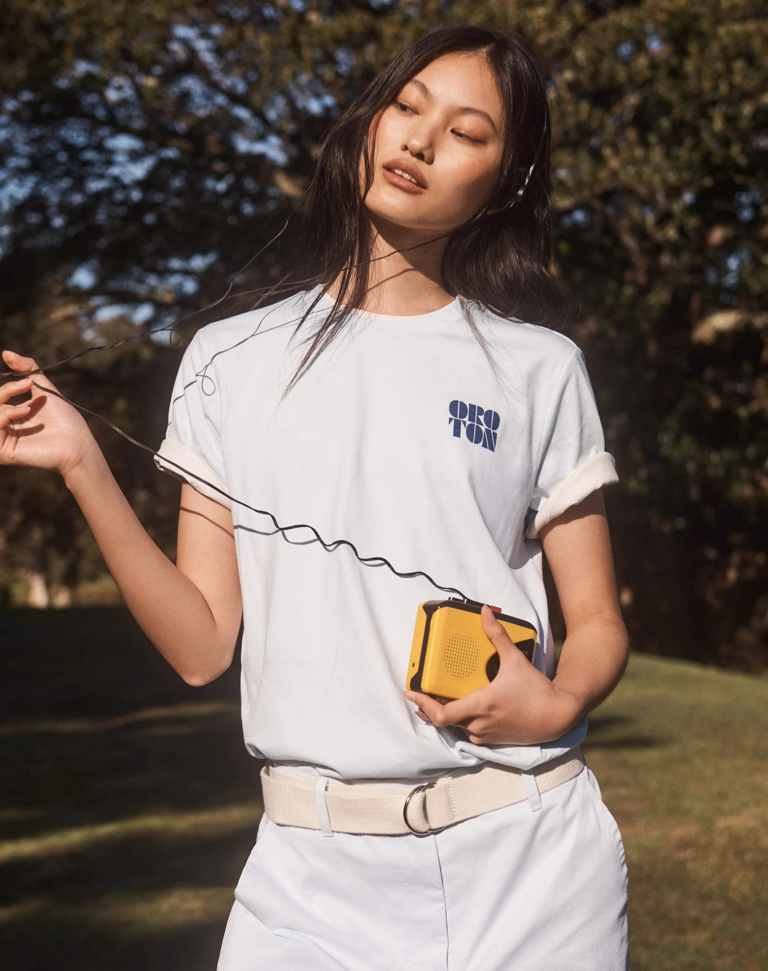 A young woman in a white t-shirt holding a yellow bag outdoors.