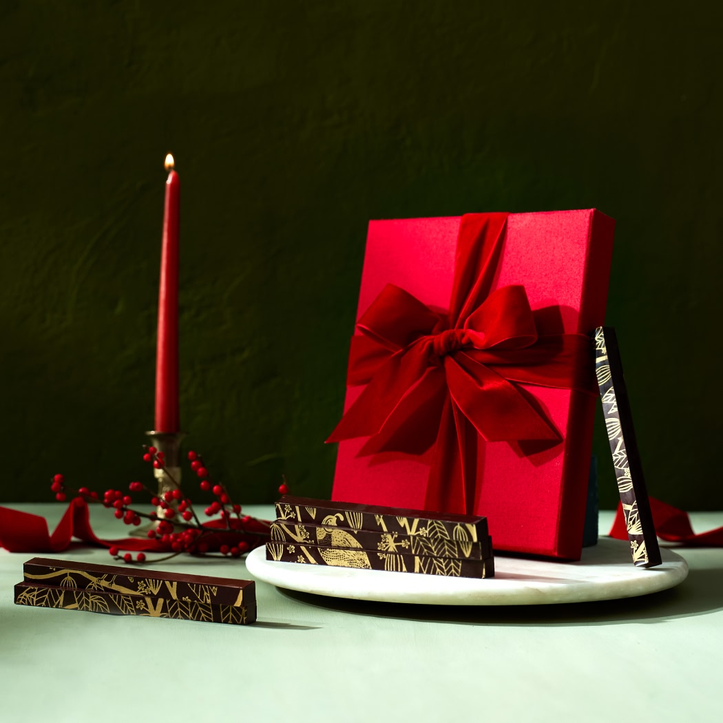 Red gift box with ribbon, chocolate bars, and a candle on a plate.