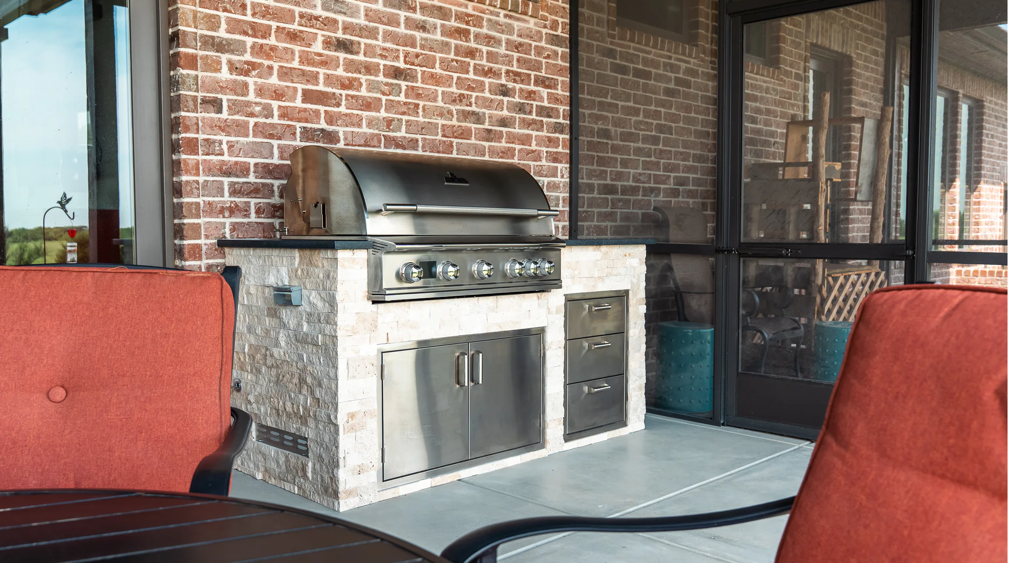 Outdoor patio with a grill and red chairs.