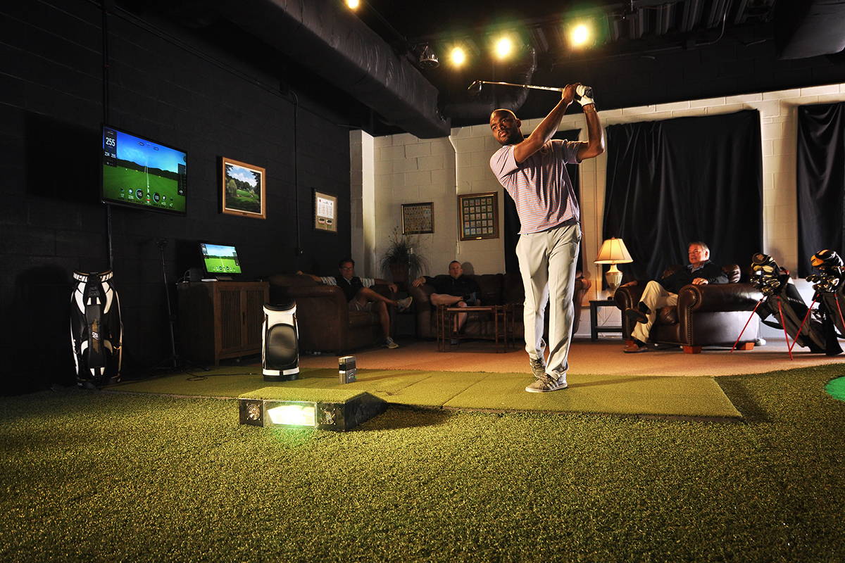A golfer swinging in a home golf simulator with the SkyTrak golf launch monitor