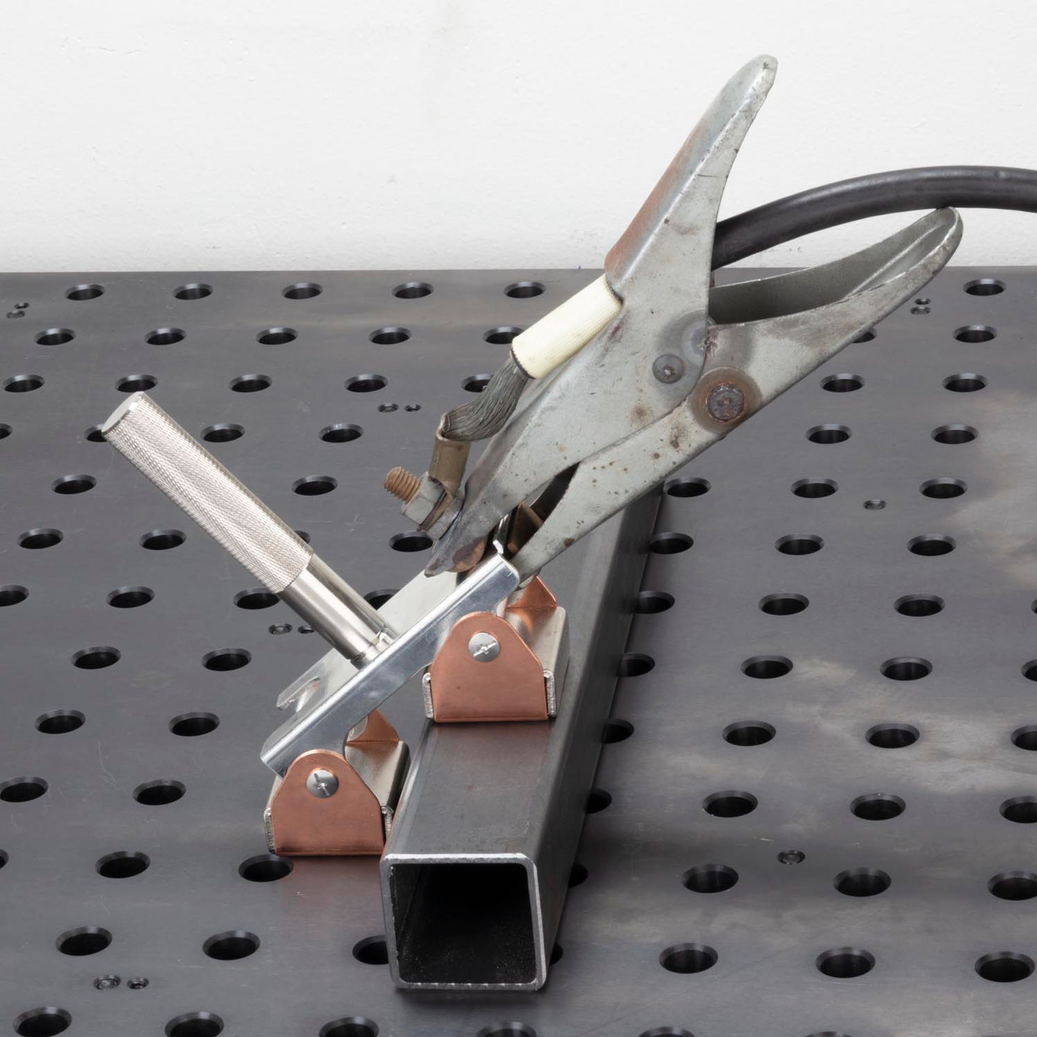 Welding clamp on a metal work surface with a cable attached.
