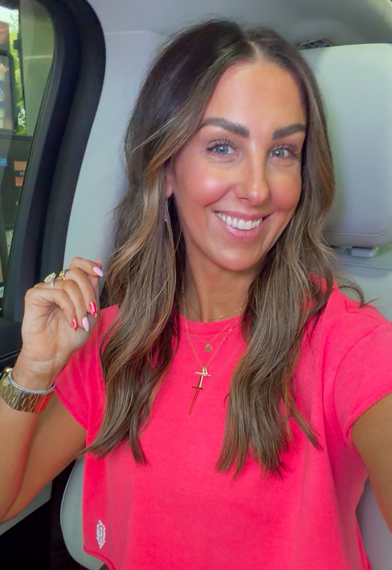 Smiling person in a pink shirt sitting in a car.