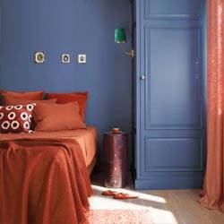 Benjamin Moore Color of the Year 2024 is a shade of blue as seen on a bedroom wall with a bed and curtains in a clay color.