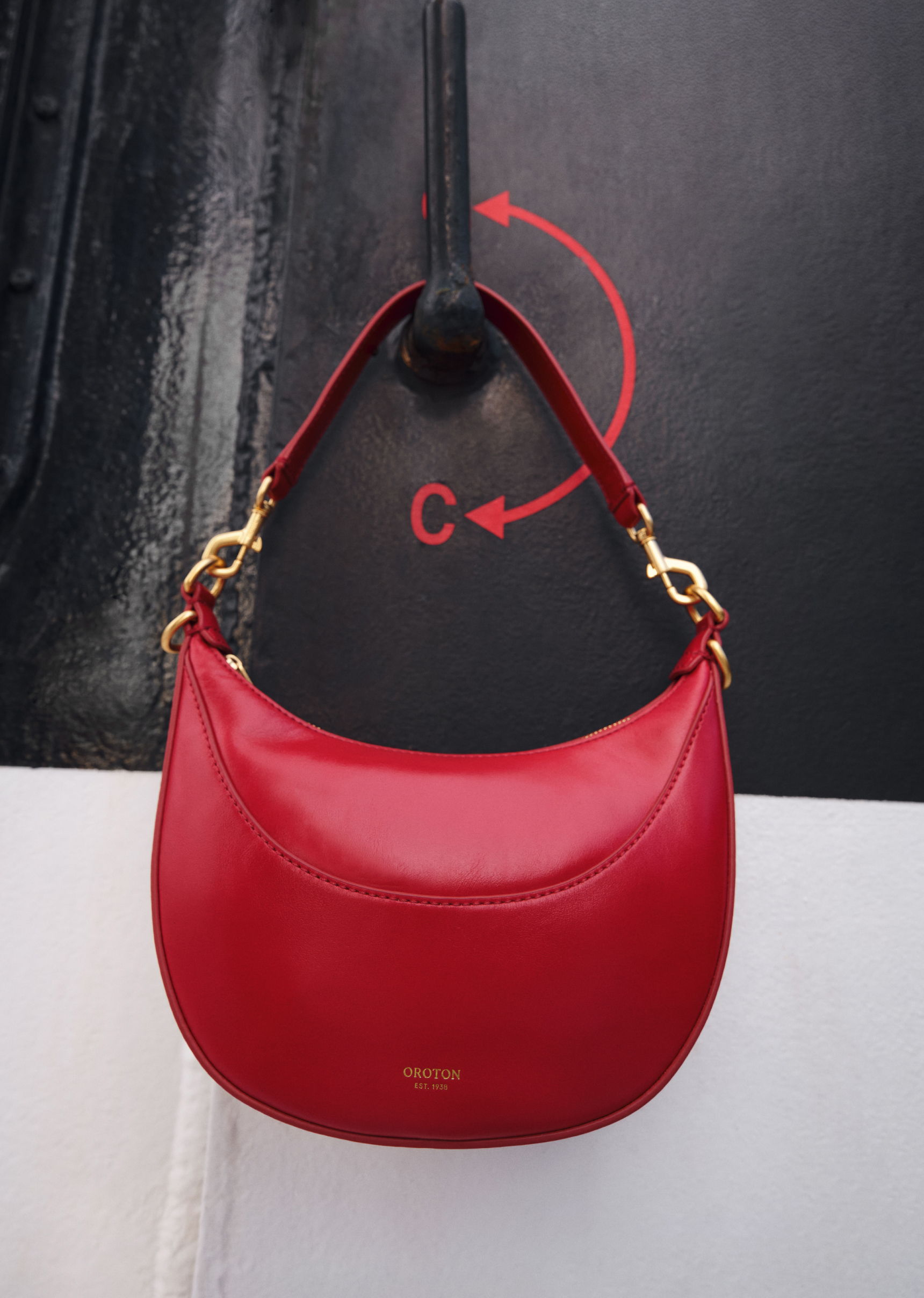 A red handbag hanging on a hook against a black background.