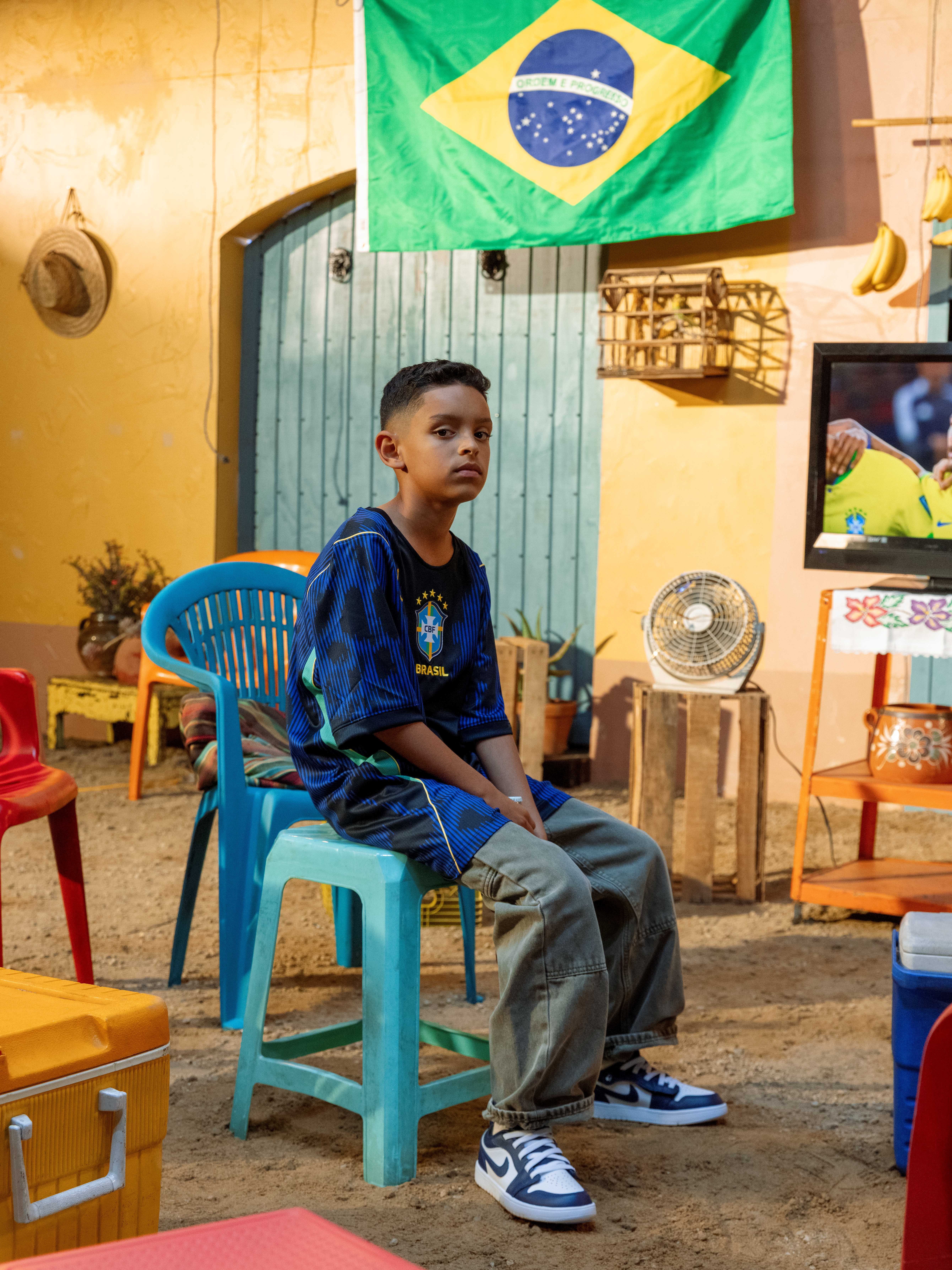 Boy sitting on a chair in a colorful room with a Brazil flag.