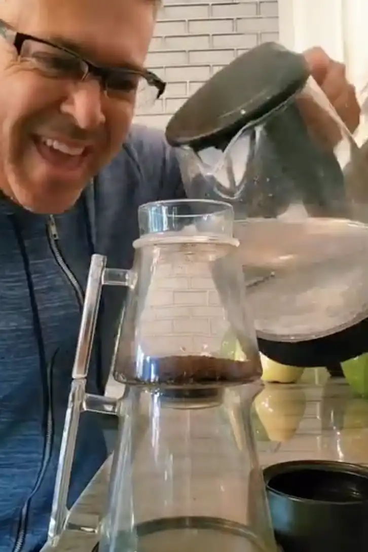 Person brewing coffee with a pour-over setup, smiling and pouring water.