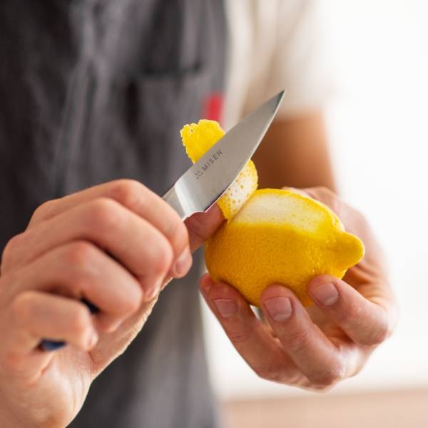 A chef uses a blue Misen Paring Knife to easily peel a lemon.