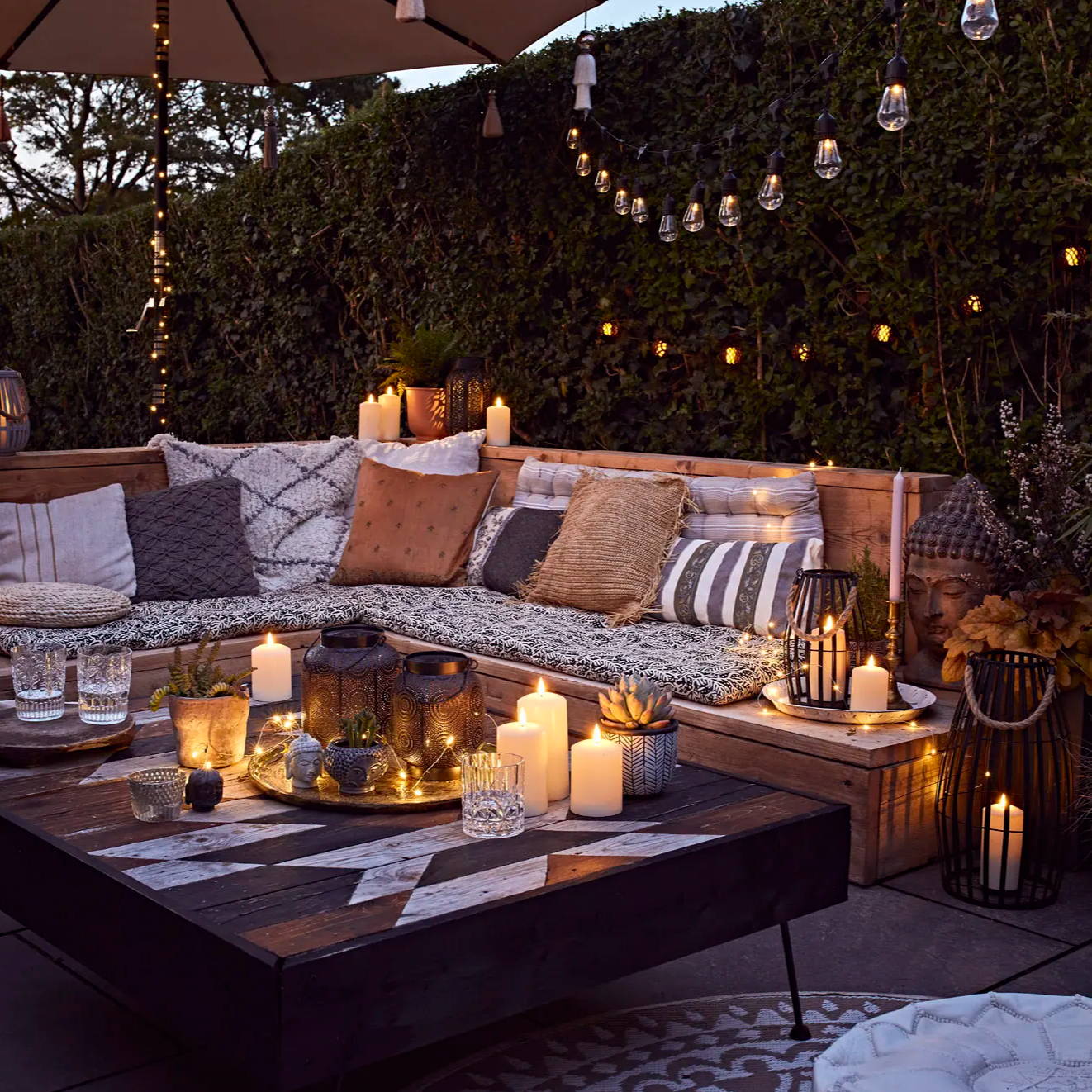 A cosy outdoor seating area with cushions, a rug and candles all decorating their outdoor space.