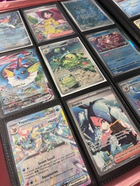 A close-up of a Pokémon TCG binder page showcasing a vibrant blue-themed collection including Vaporeon VMAX, Vaporeon ex, and full-art Trainer cards like Dendra and Parasol Lady.