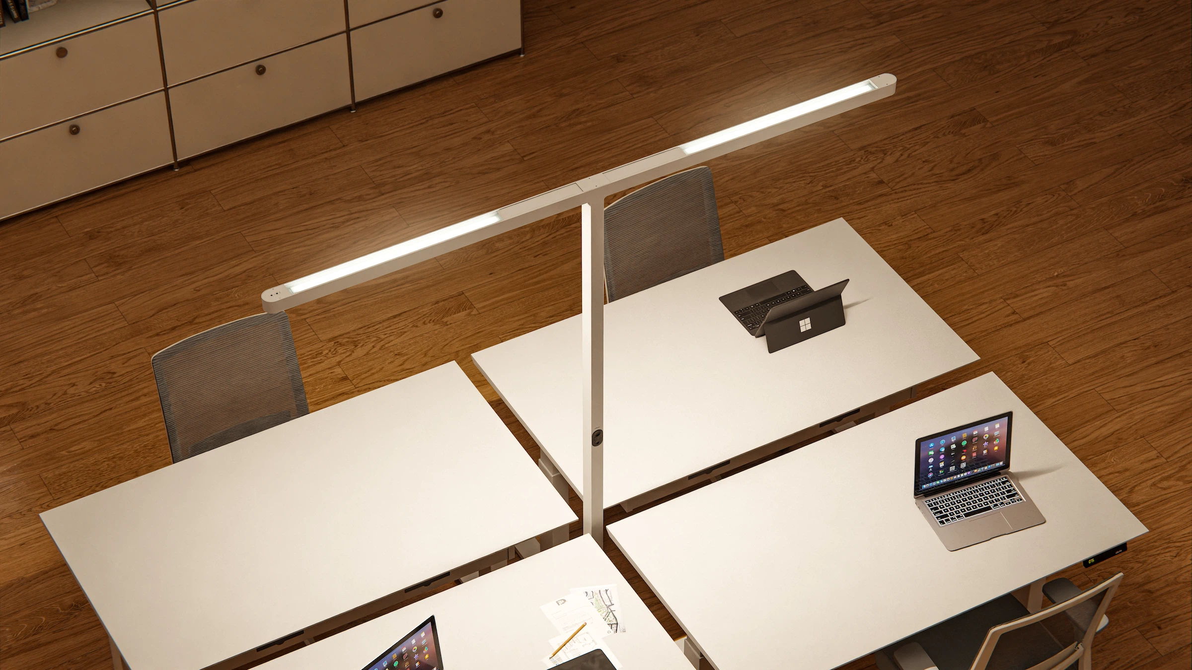 A bird's-eye view of the white " Lumino " Pro Duo floor lamp, positioned in the center of a group of four desks in an office.